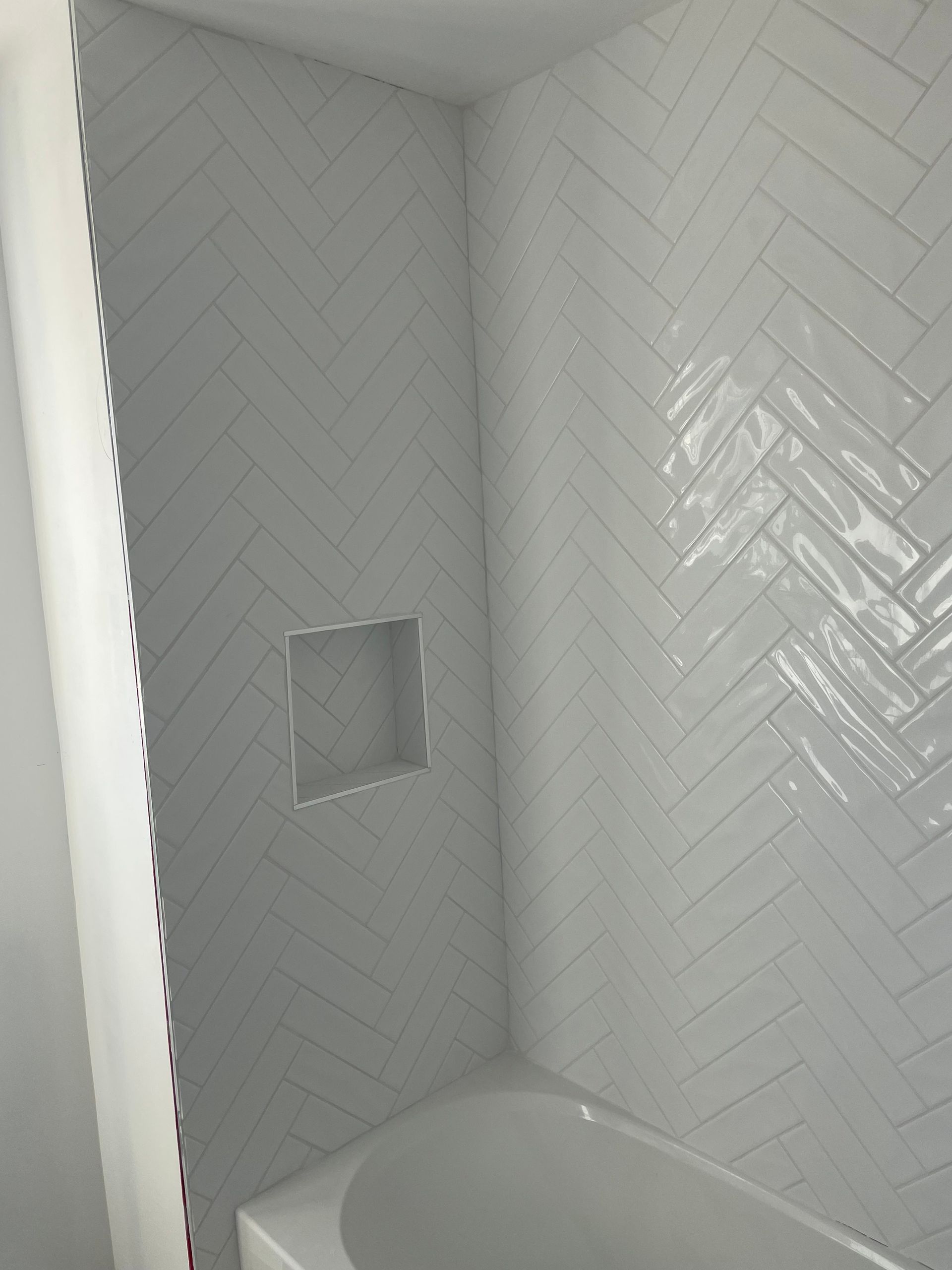 White tiled shower stall with built-in niche and tub edge.
