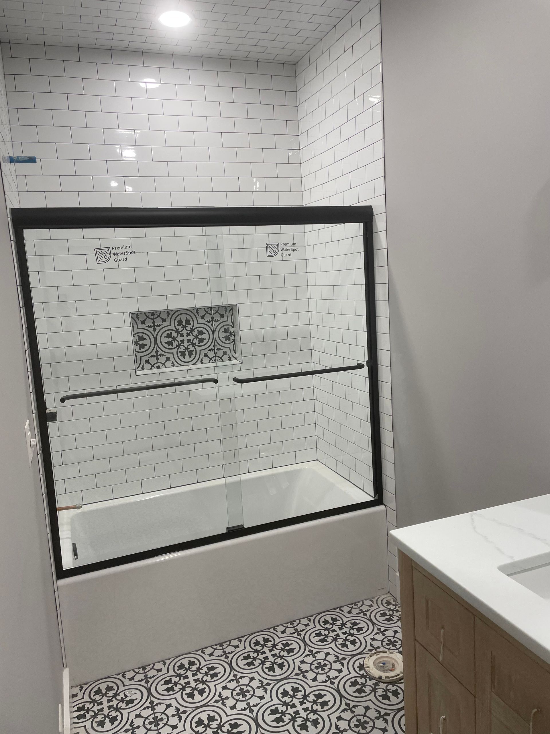 Small bathroom with patterned tile, glass shower enclosure, and wood vanity countertop.