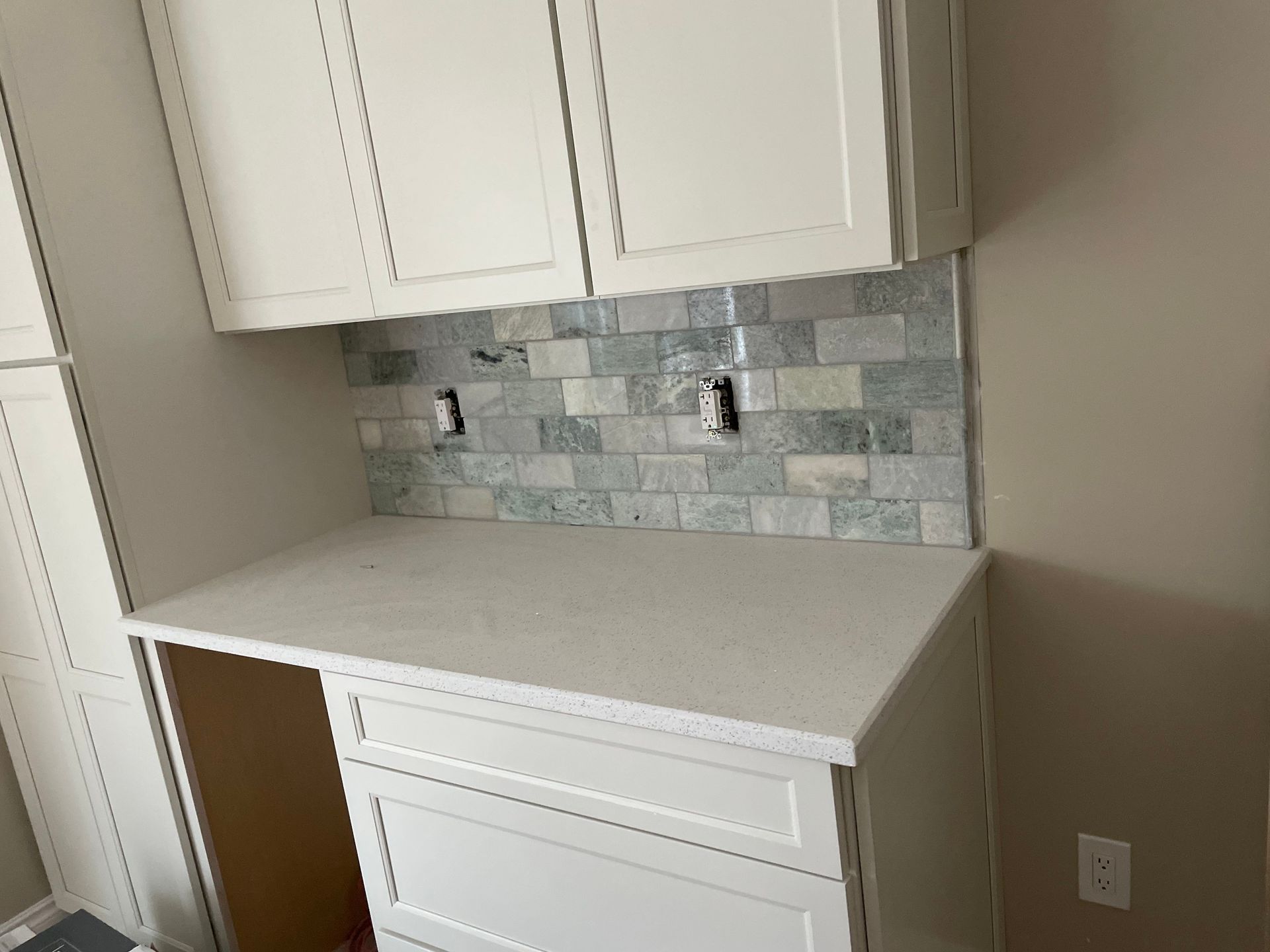 Kitchen nook with white cabinets, light countertop, and blue-gray tile backsplash above a lower cabinet.