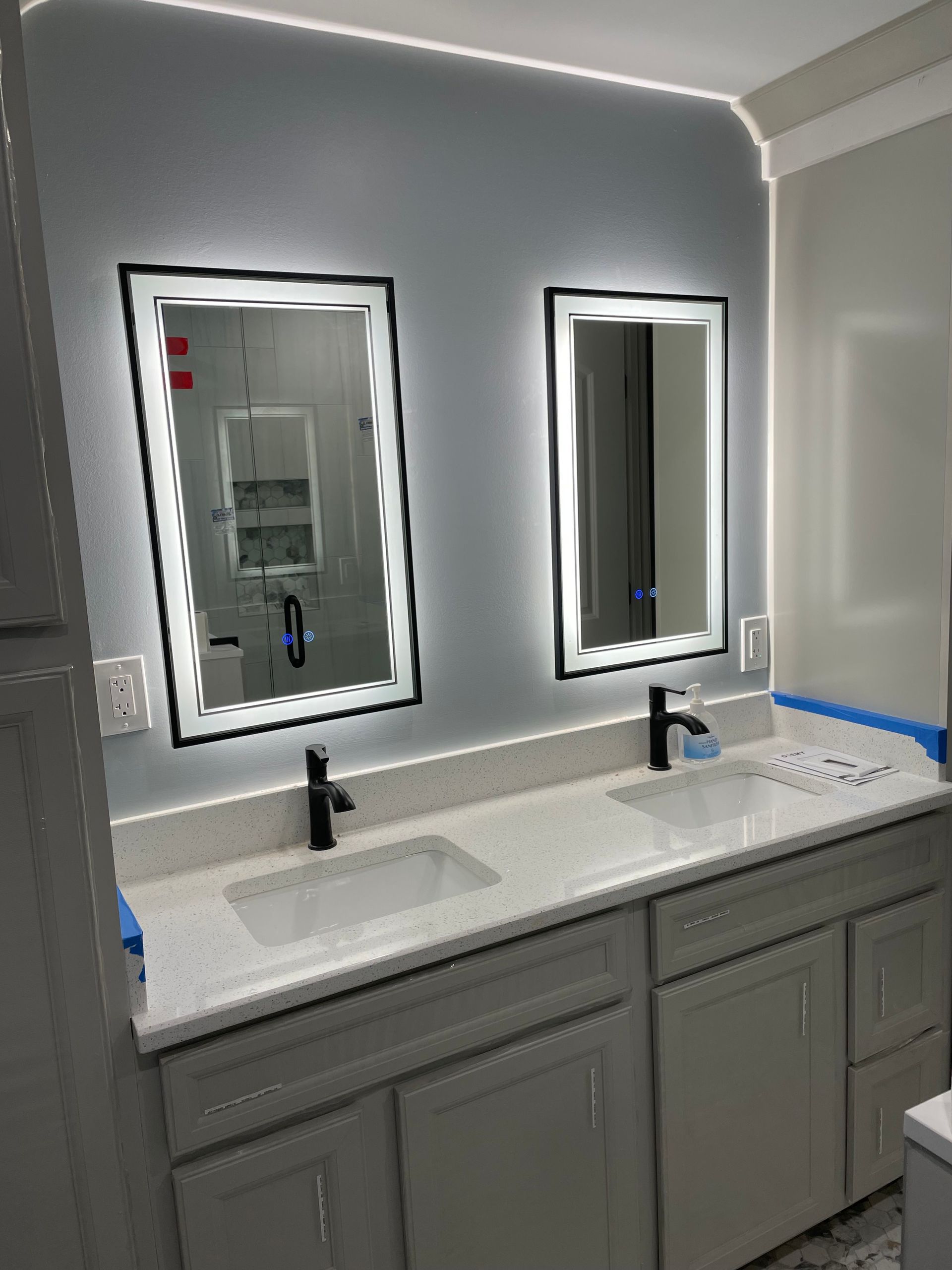 Modern bathroom vanity with two sinks, mirrors, and black faucets under bright LED lighting
