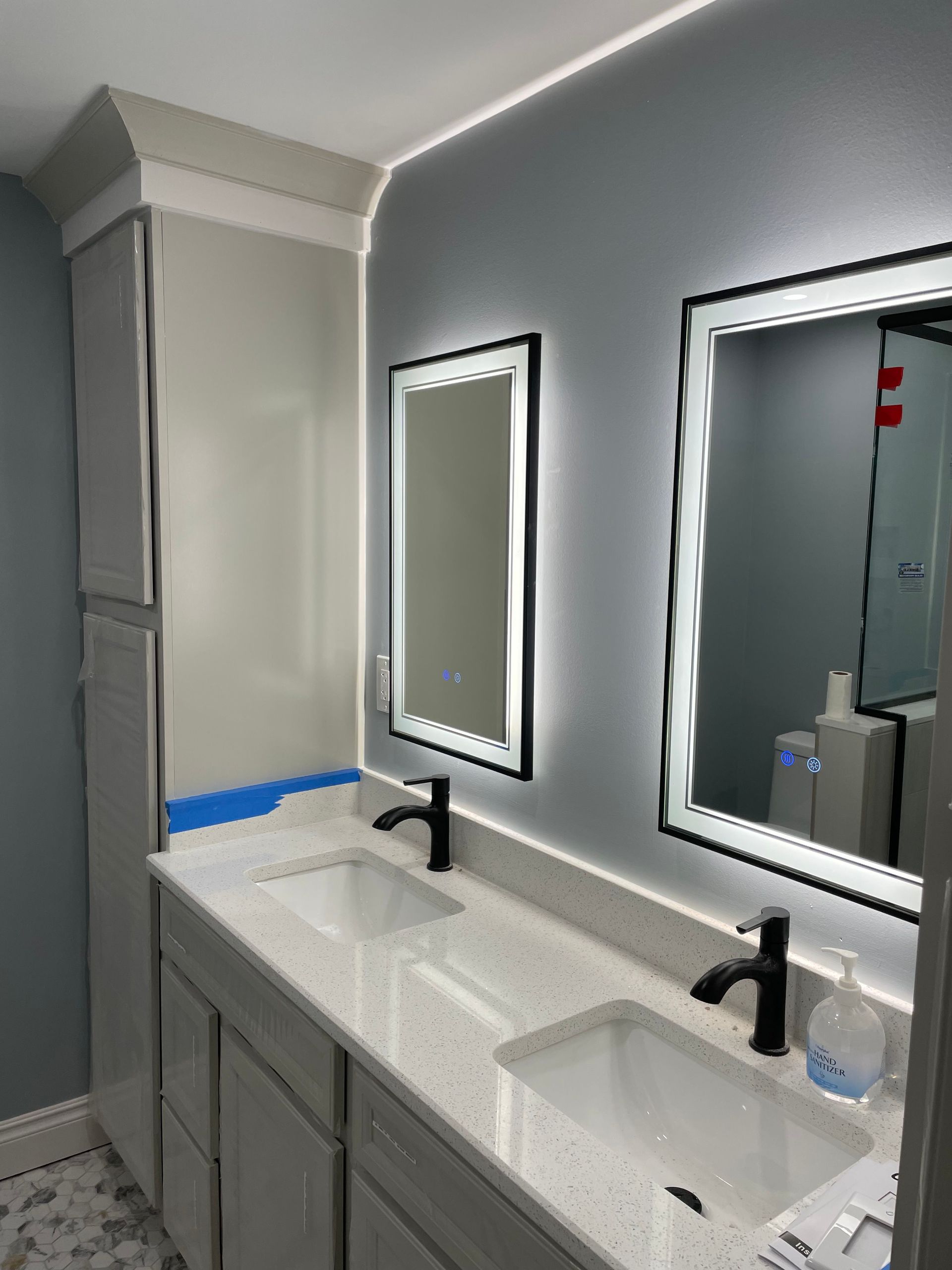 Double vanity bathroom with gray cabinets, black faucets, mirrors, and white countertops.