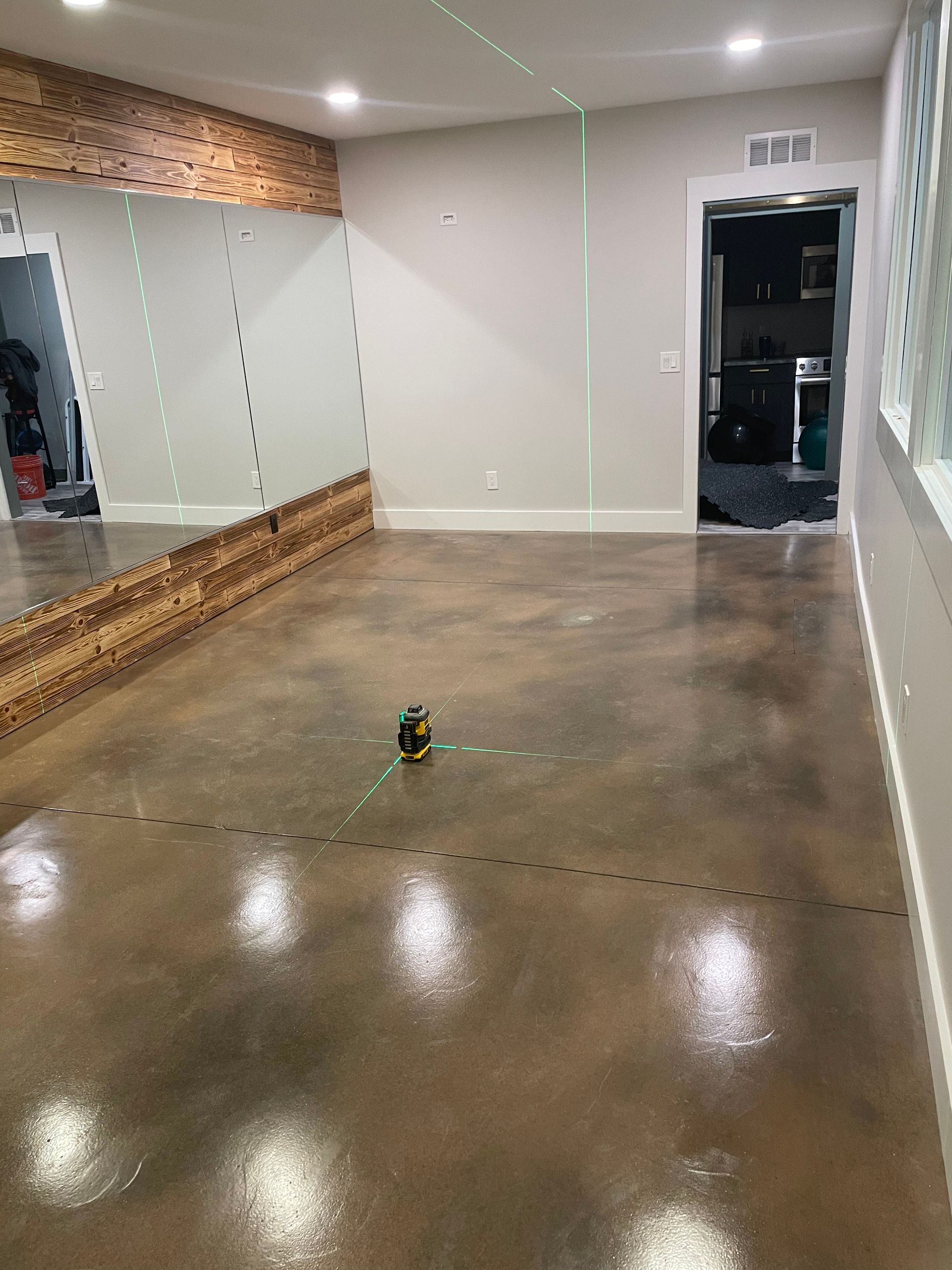 Empty dance studio with mirrored wall, polished concrete floor, and doorway to a back room.