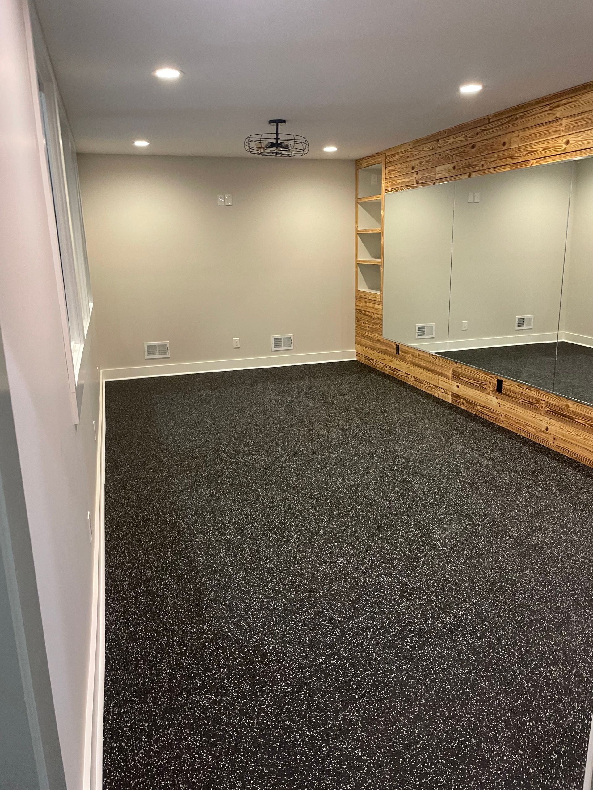Empty mirrored room with black speckled carpet, beige walls, and recessed ceiling lights