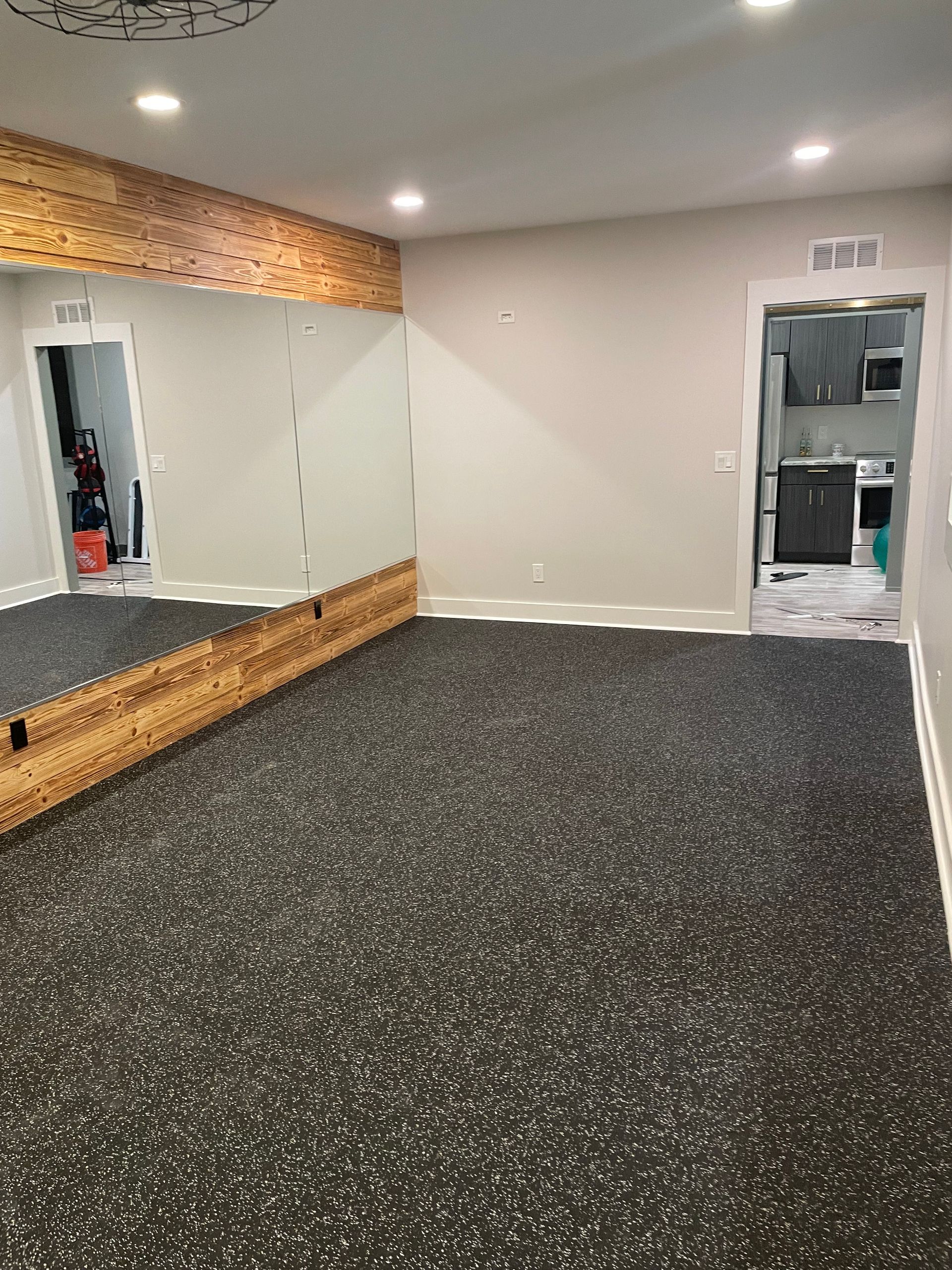 Empty mirrored room with speckled carpet, white walls, and a doorway to a kitchen area.
