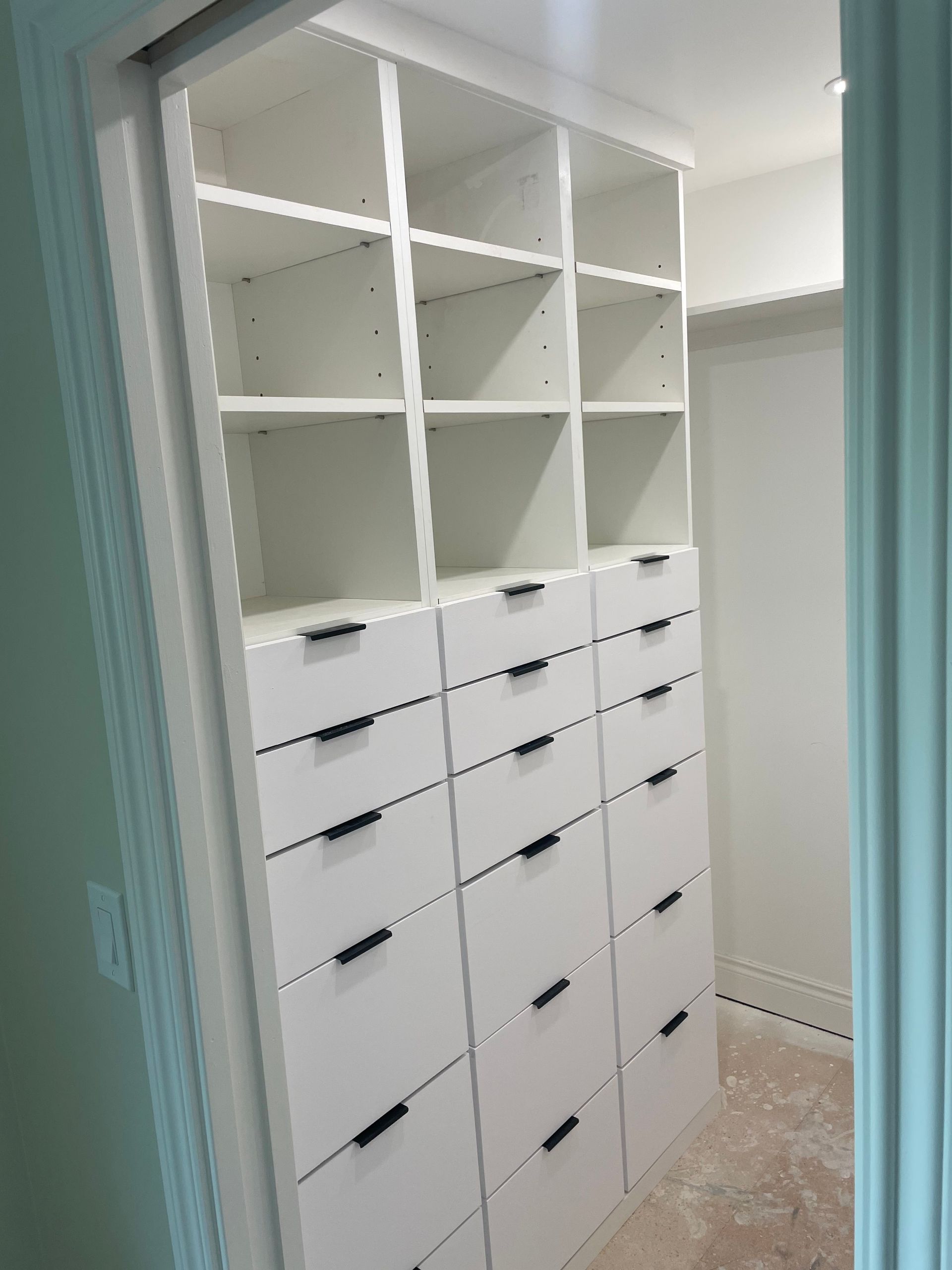 White built-in closet with open shelves and drawers in a narrow hallway, with a closet rod on the right.