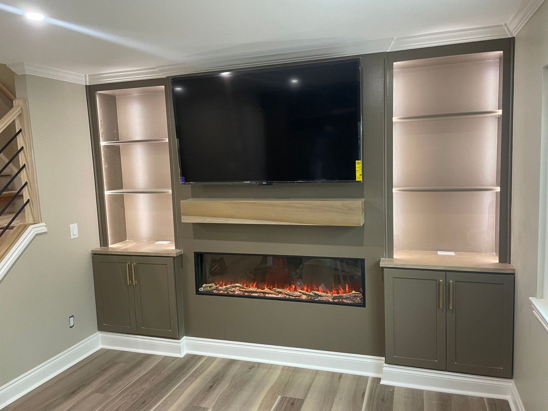 Built-in fireplace wall with TV, lit shelves, and dark cabinets in a modern living room