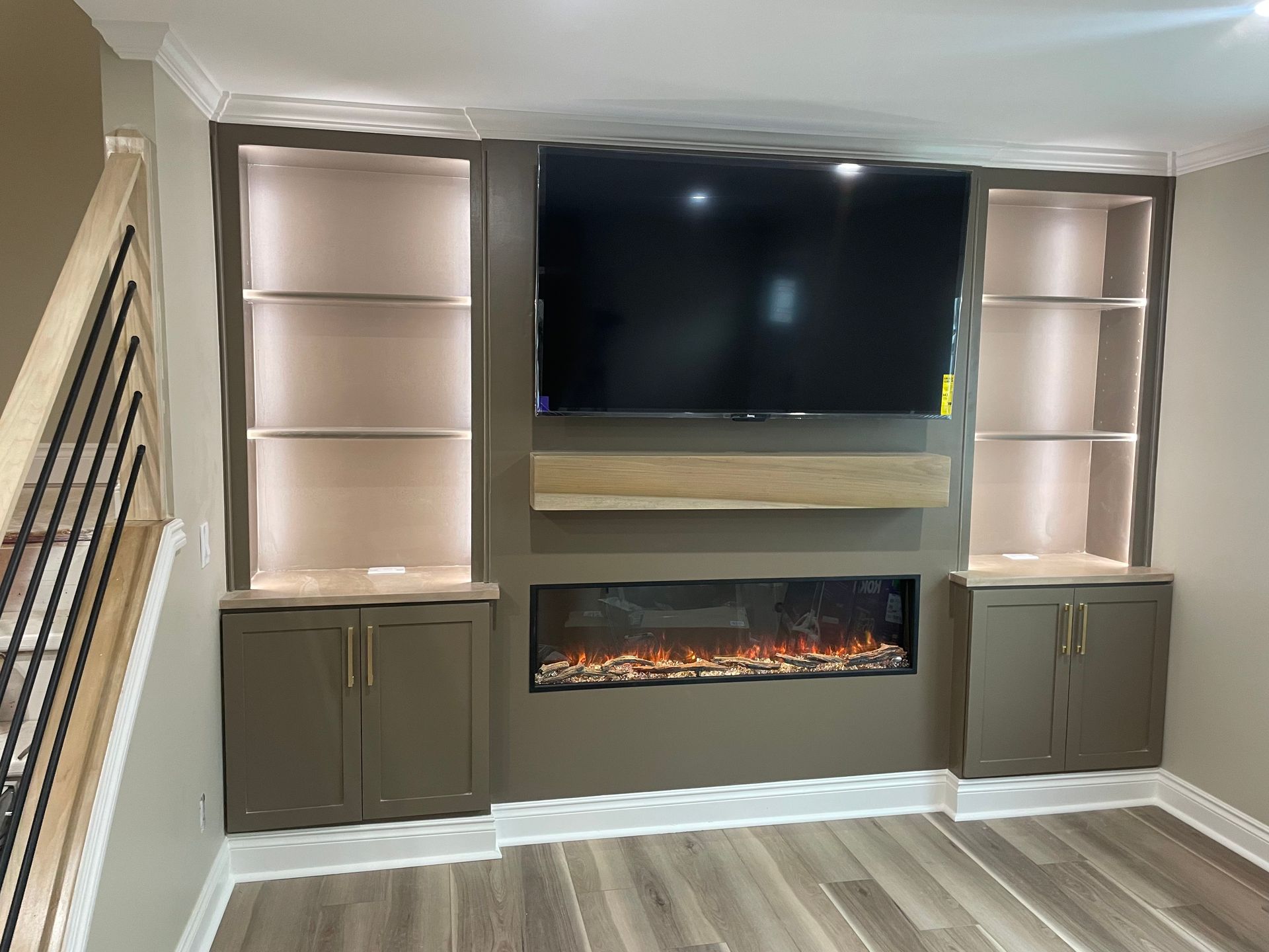 Built-in living room media wall with TV, electric fireplace, and backlit cabinets