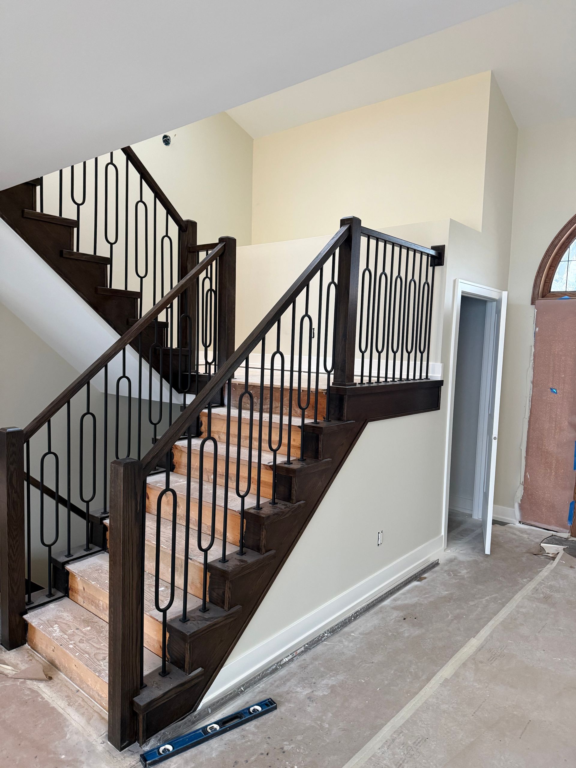 Indoor staircase with dark wrought-iron railings and brick steps under construction, beside a doorway and bare walls