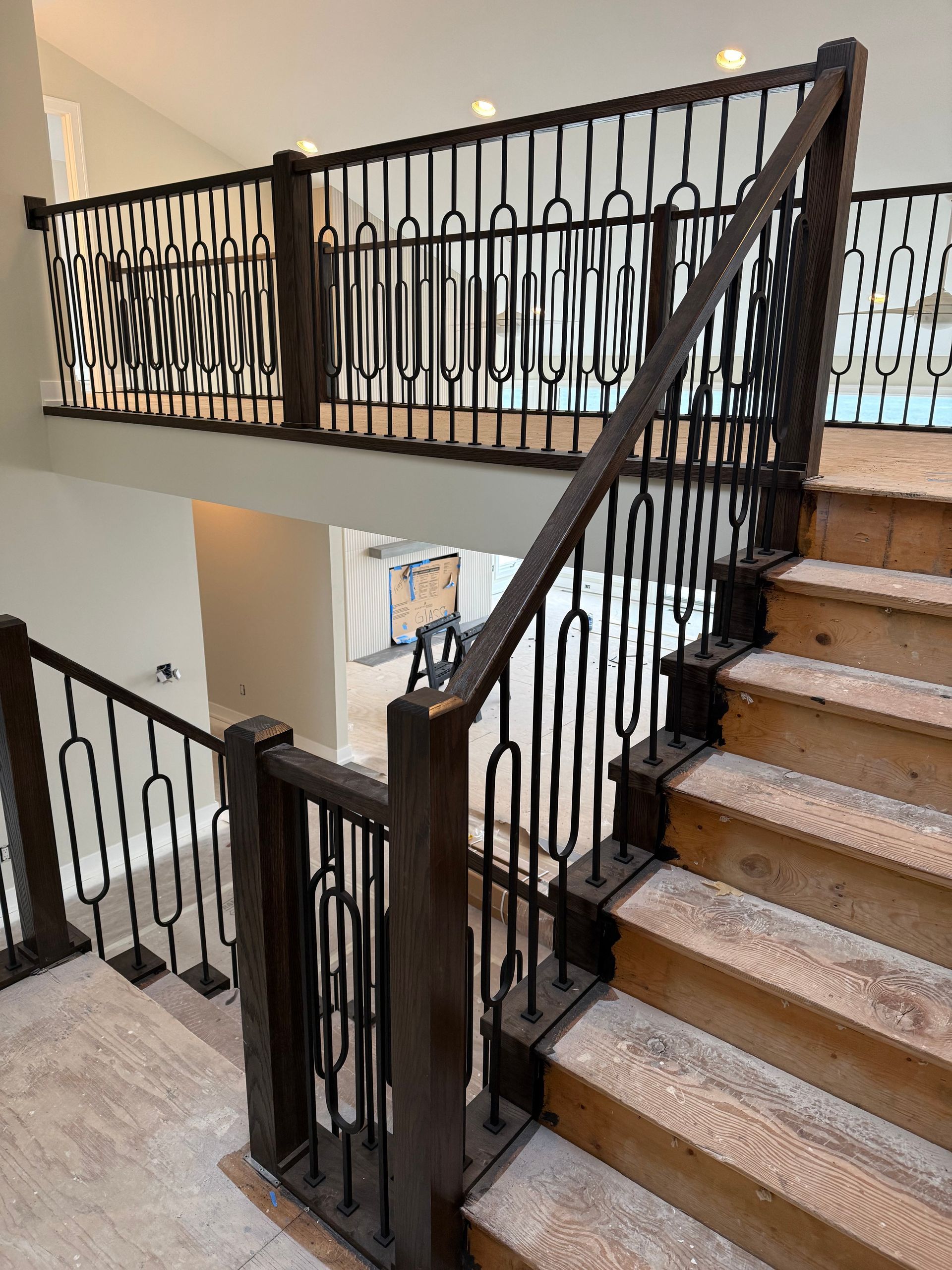 Indoor staircase with beige carpet, dark iron railings, and a landing overlooking the lower floor