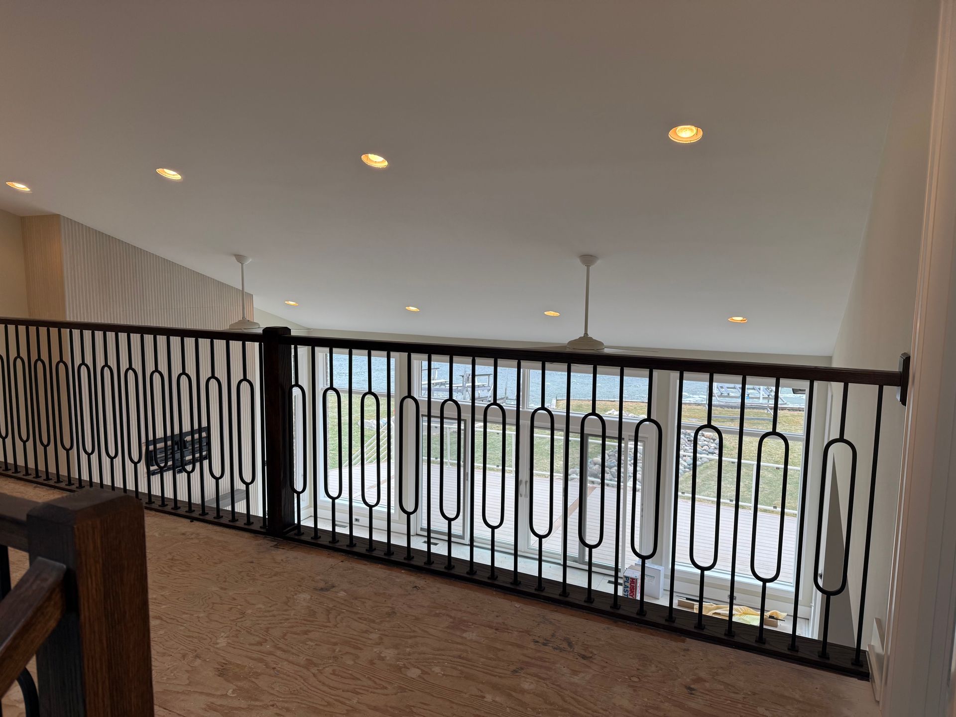 Indoor balcony with black railing and recessed ceiling lights overlooking a bright exterior.