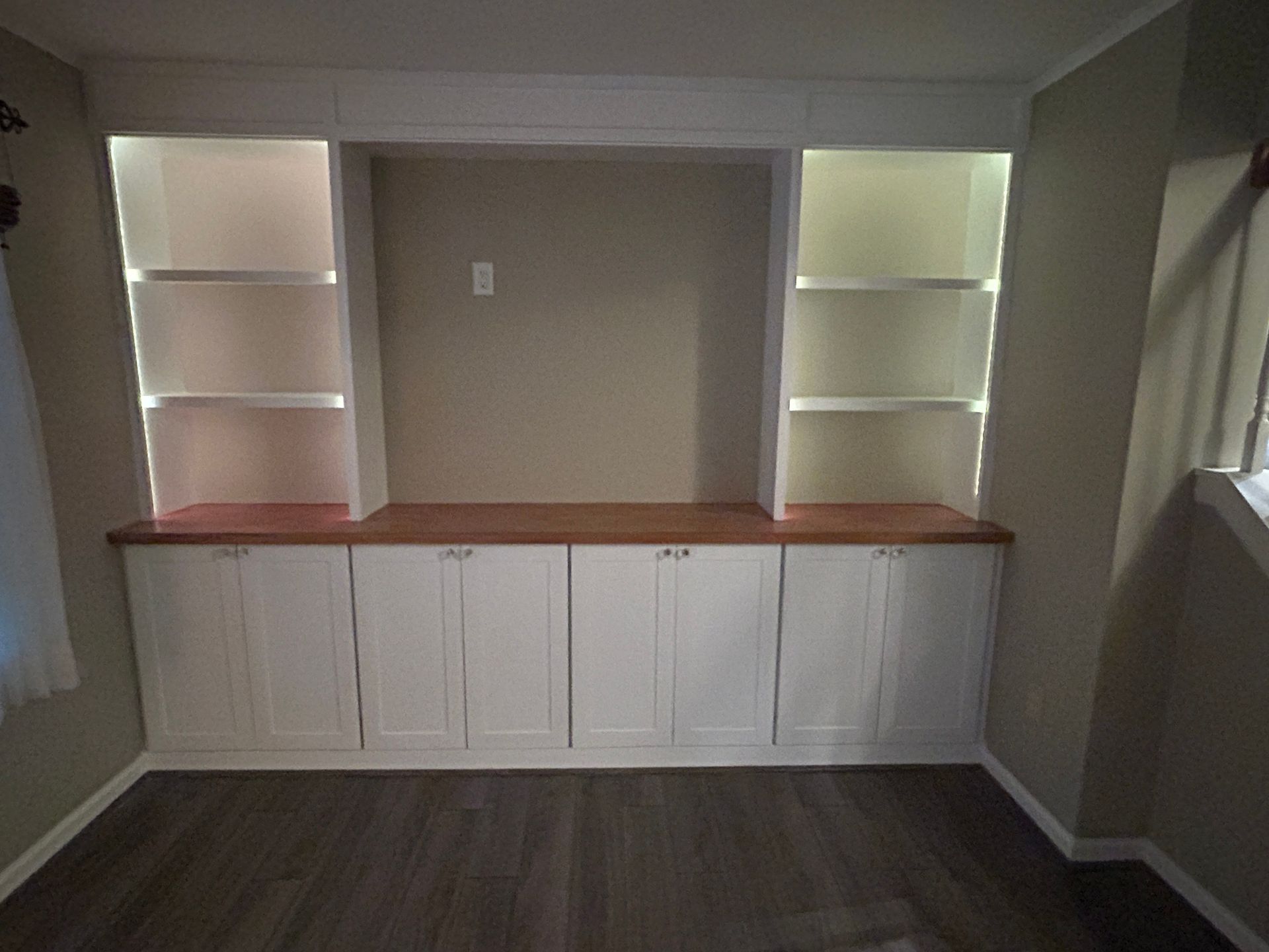 Built-in white cabinets with wood countertop and shelving in a small room.