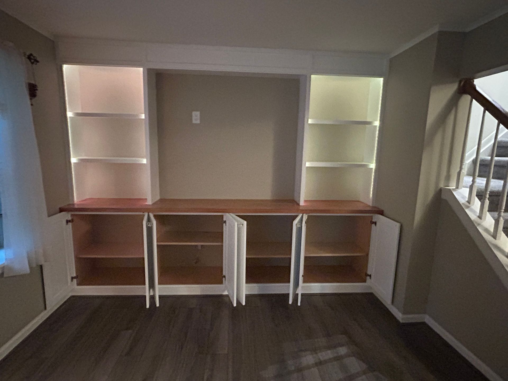 Built-in desk with white shelves and lower cabinets in a small room, with a window on the right