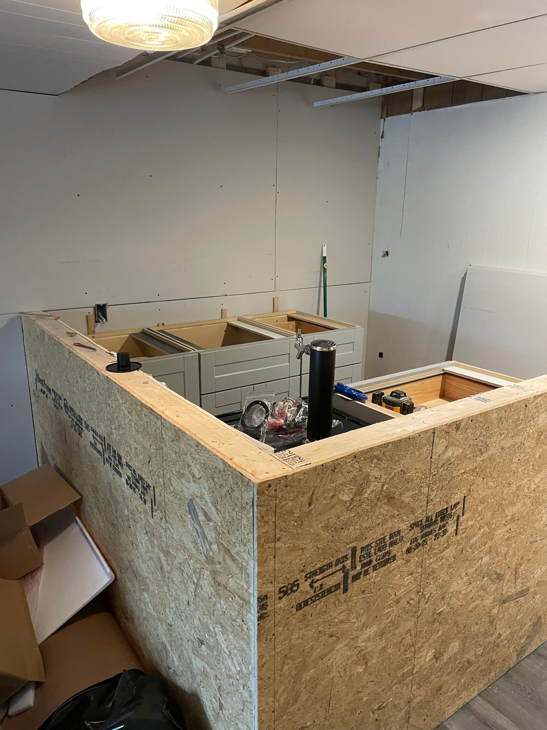 Partially built plywood enclosure in a room, with tools and ceiling panels removed above it.