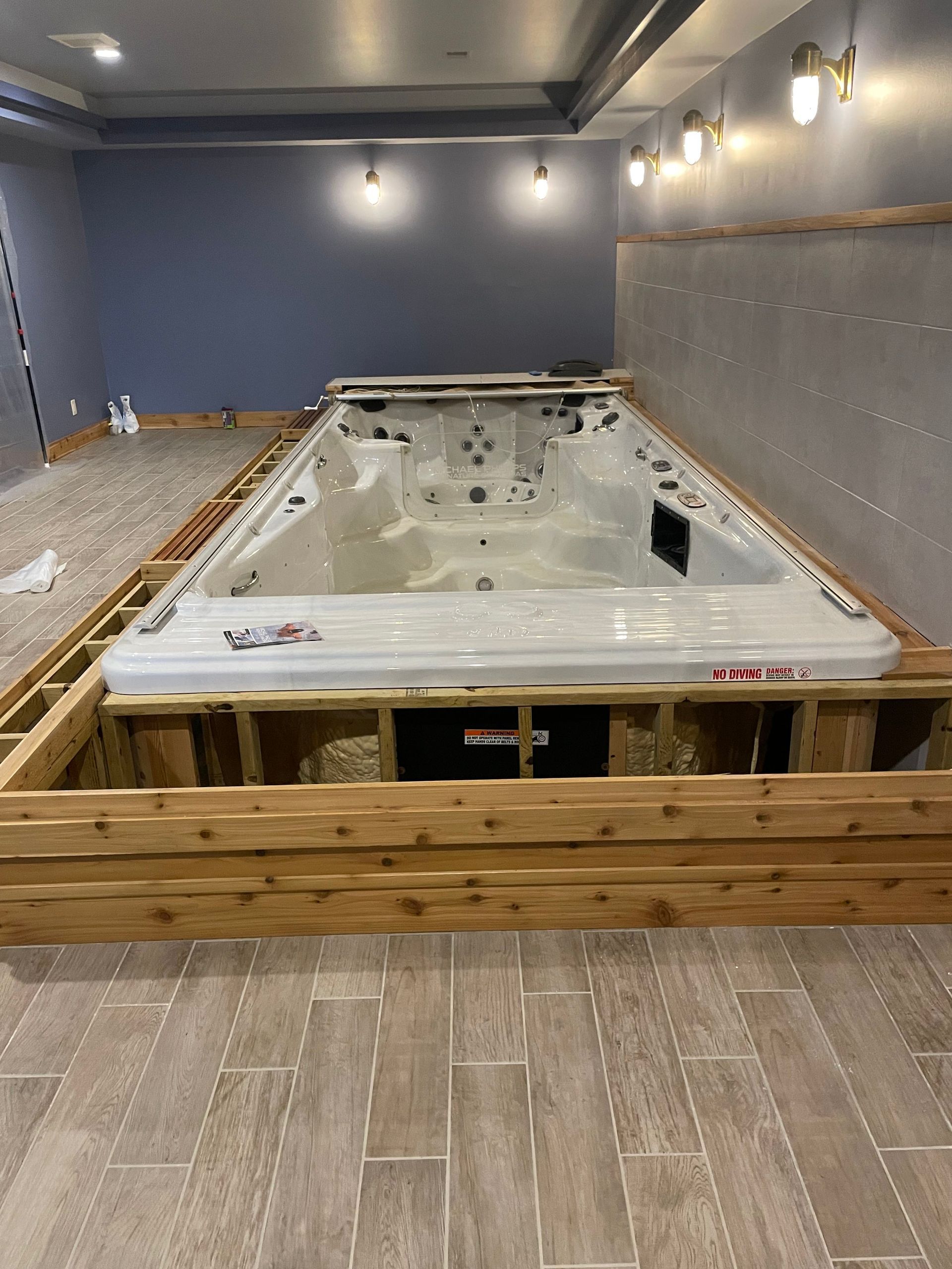 Empty indoor hot tub under construction, surrounded by wooden framing in a tiled room.