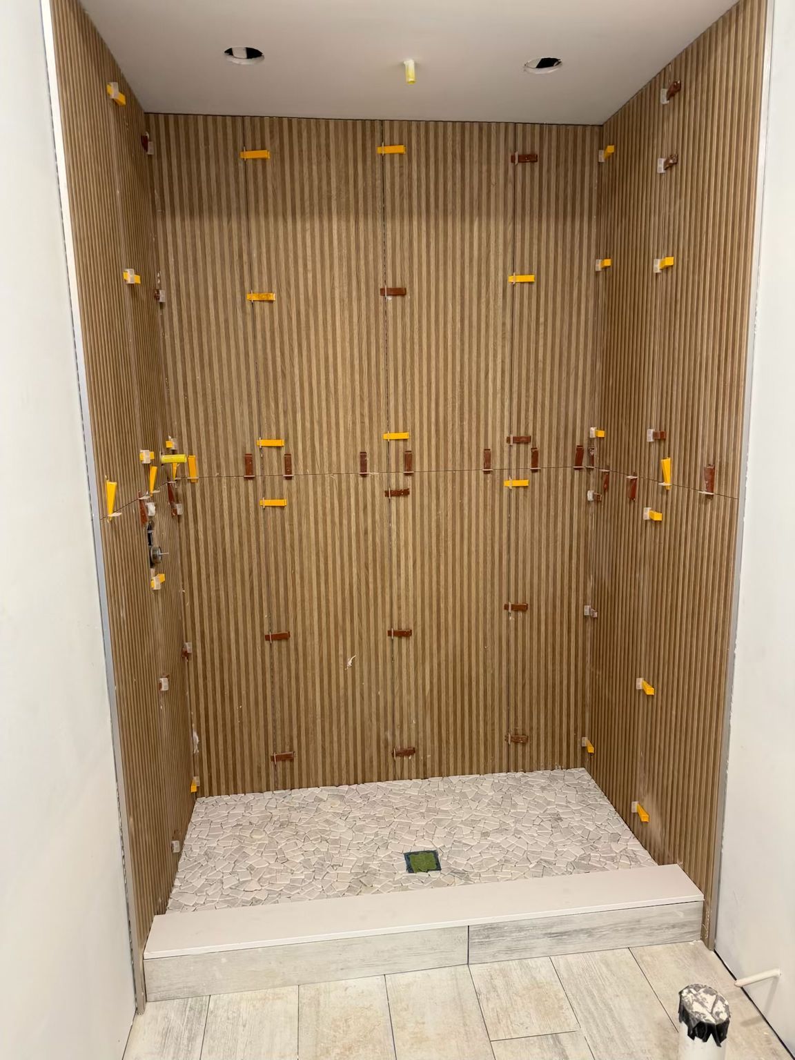 Empty tiled shower stall with wood-look wall panels and white pebble floor.