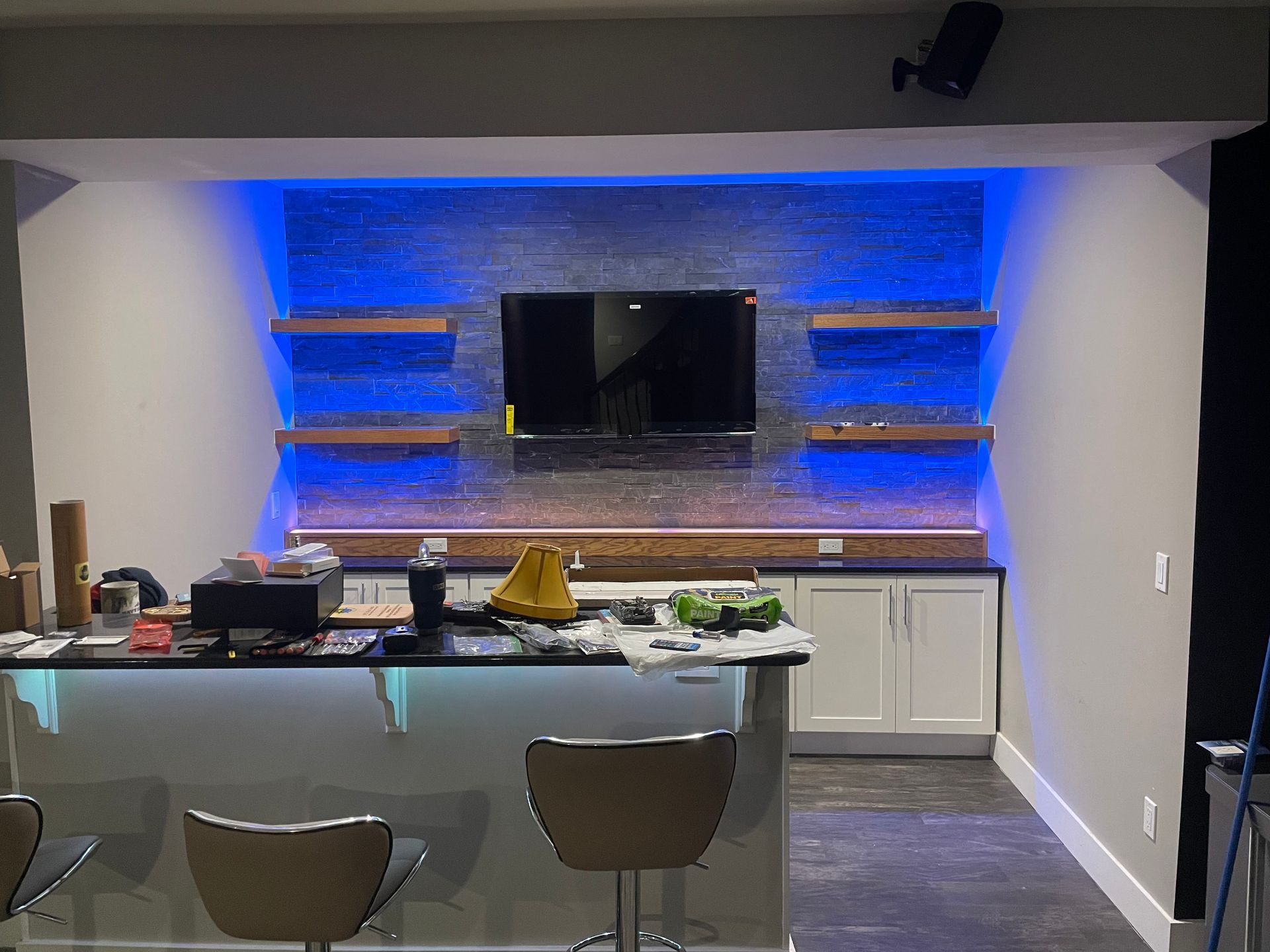 Modern kitchen with island, bar stools, and wall-mounted TV above blue-lit shelves and backsplash