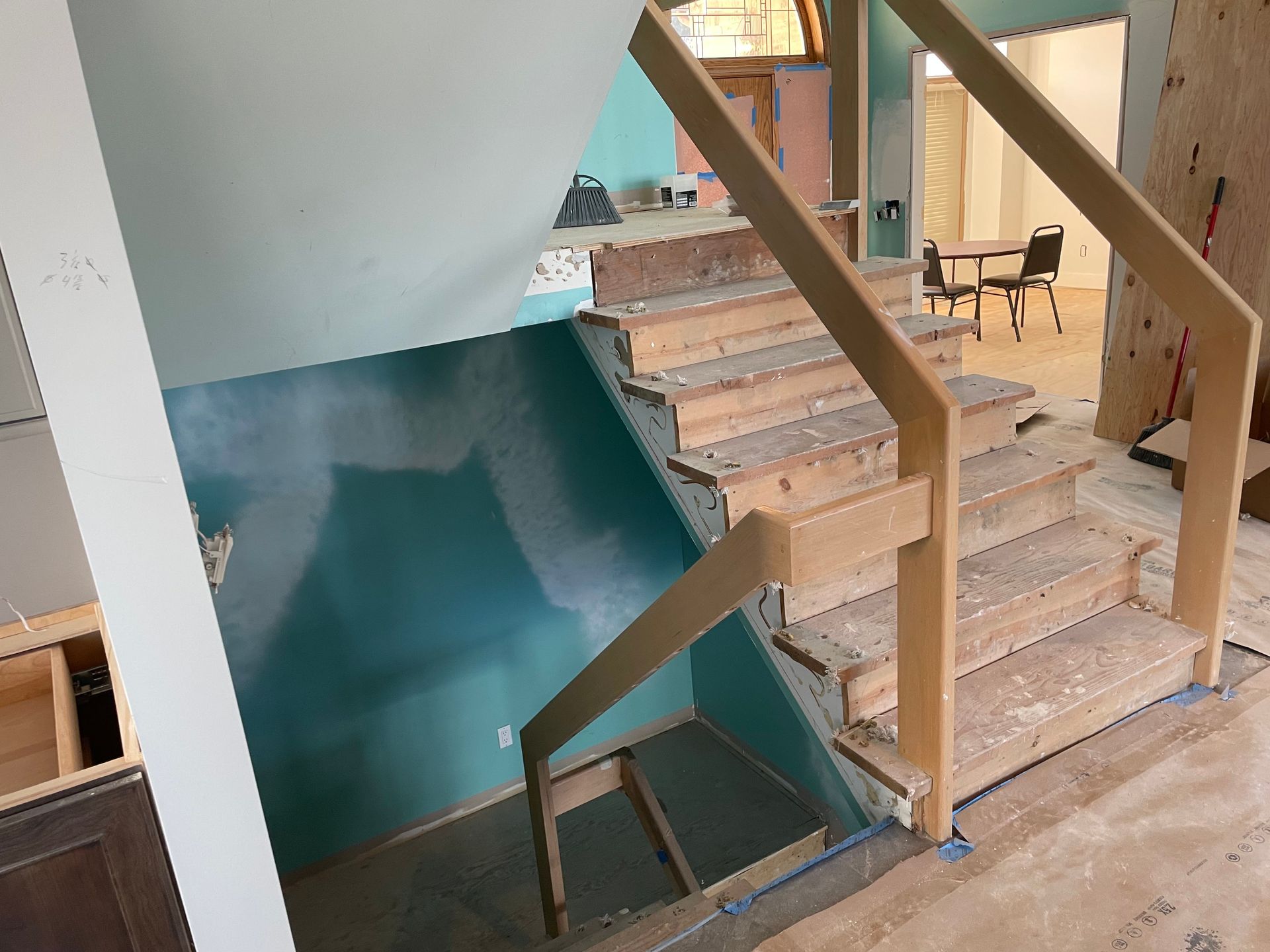 Interior stairwell with unfinished wooden stairs and teal wall paneling, viewed from the landing