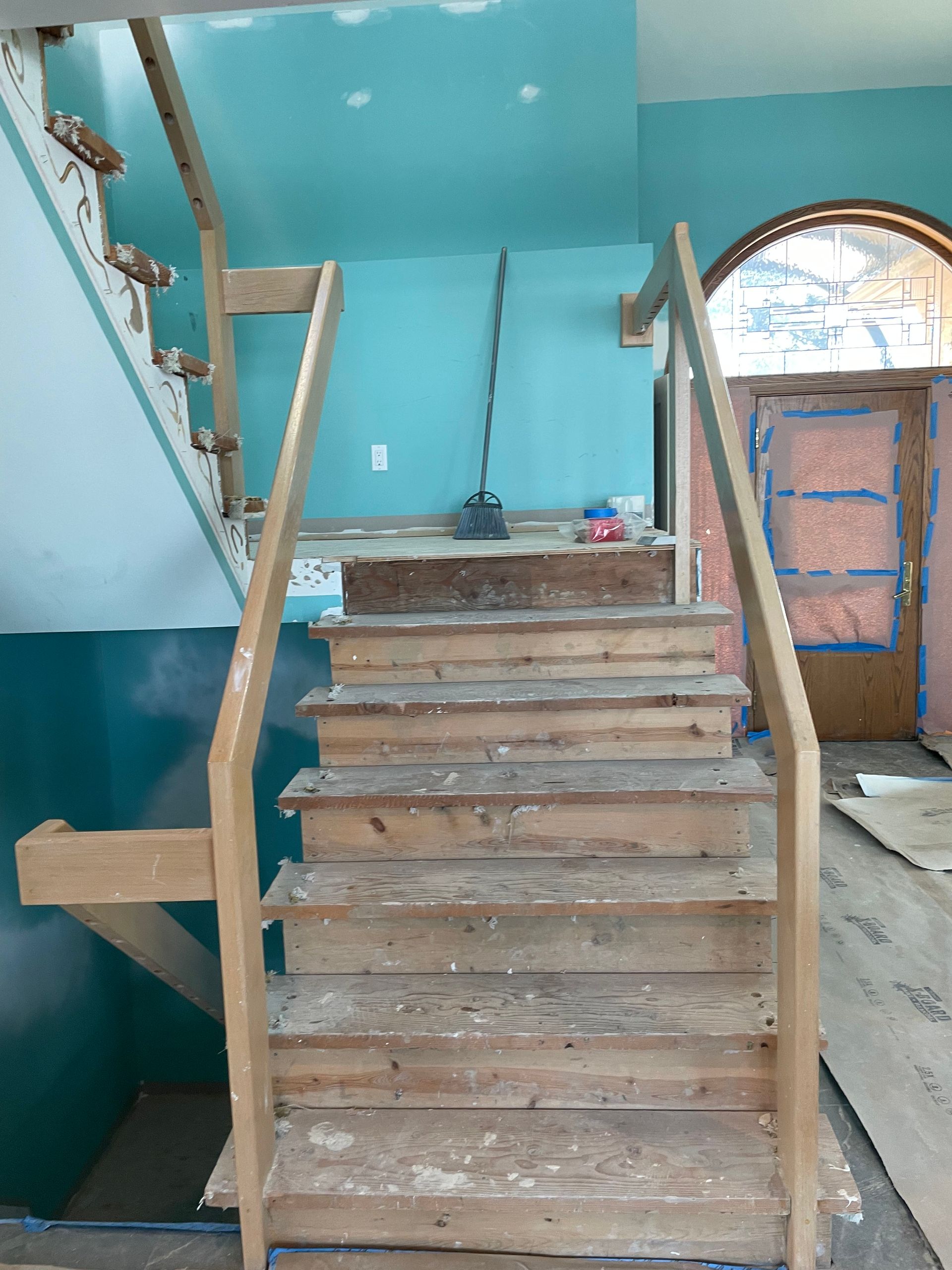 Unfinished wooden staircase inside a turquoise-painted interior with an arched doorway on the right.