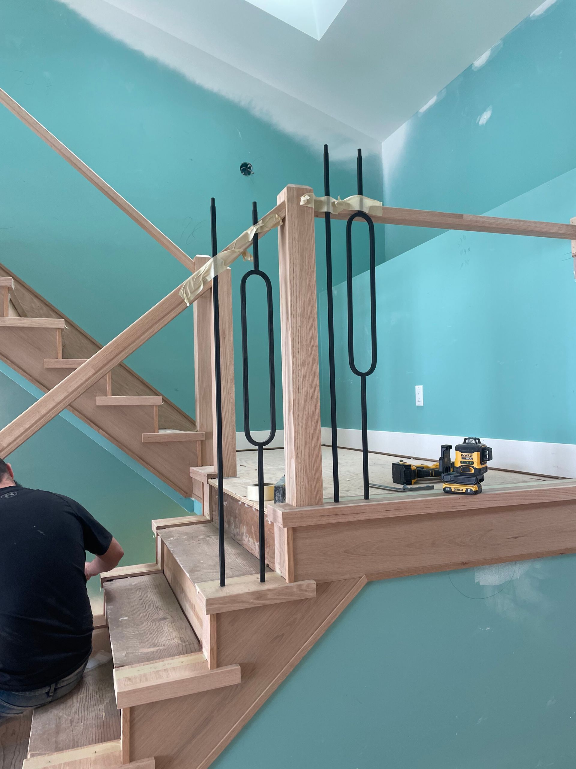 Staircase under construction with wooden railings, teal walls, and a worker on the left.