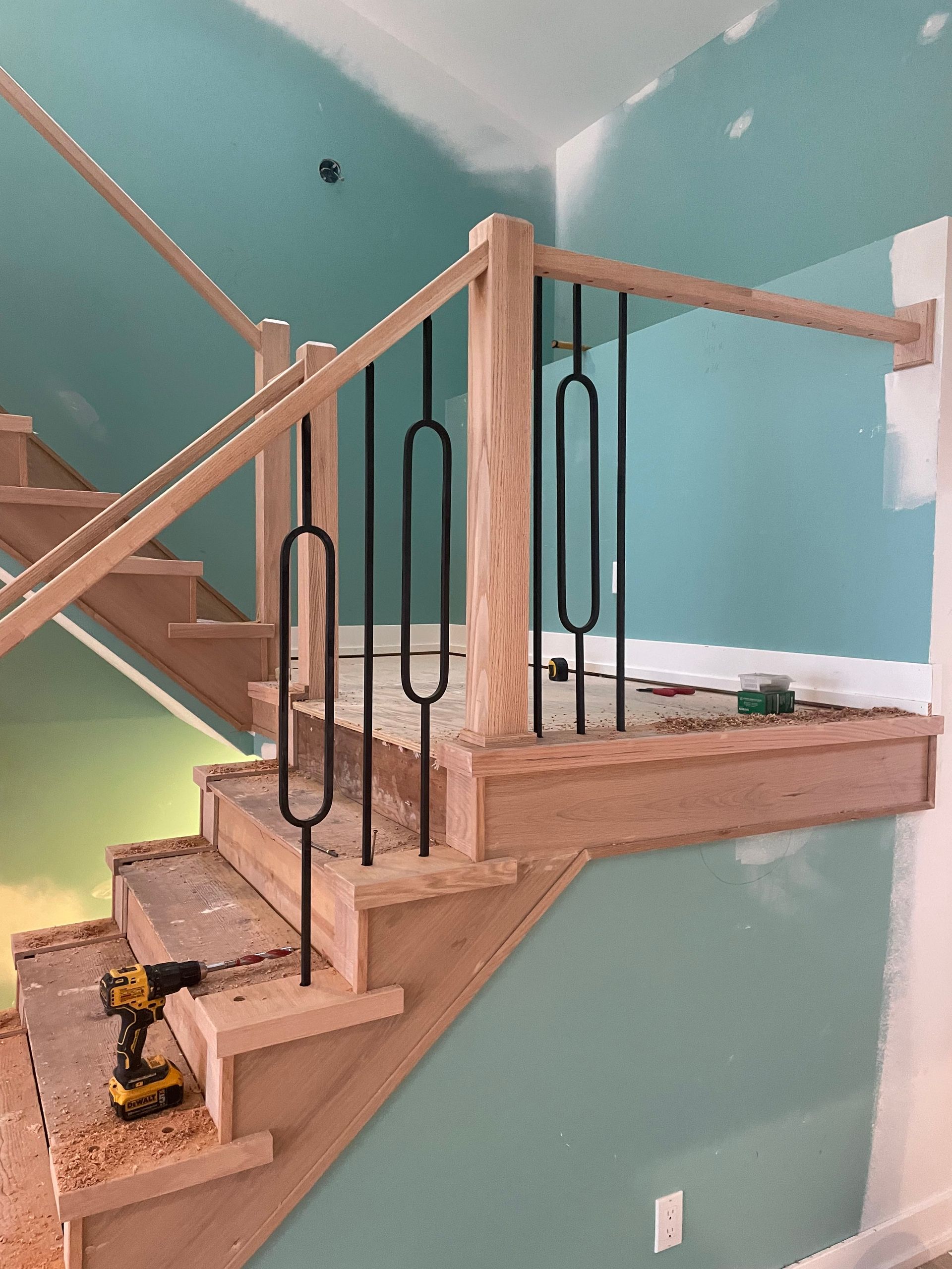 Partially built wooden staircase with black metal balusters in a teal-walled room