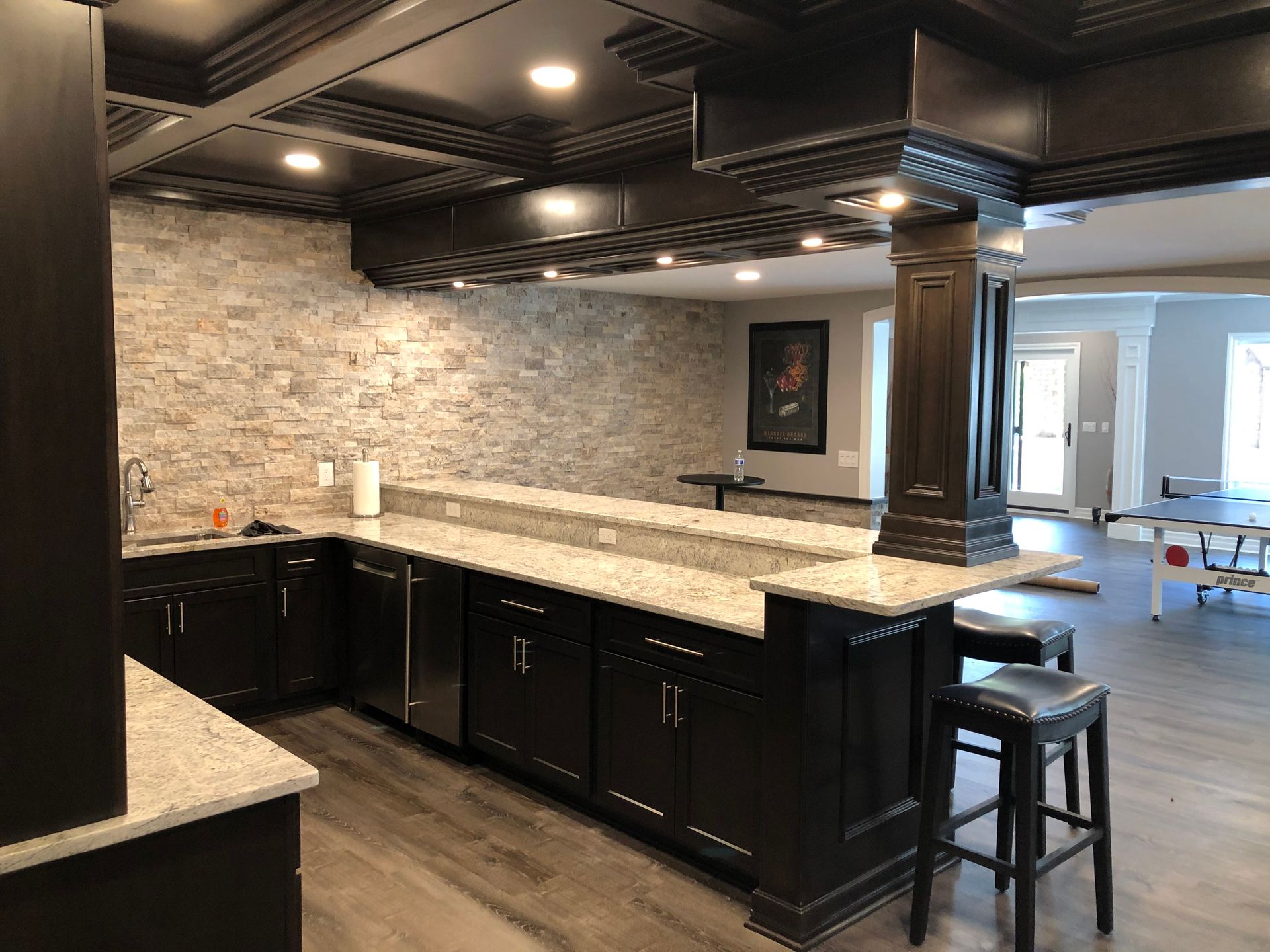 Modern kitchen with black cabinets, granite island, stone backsplash, and two bar stools in an open floor plan