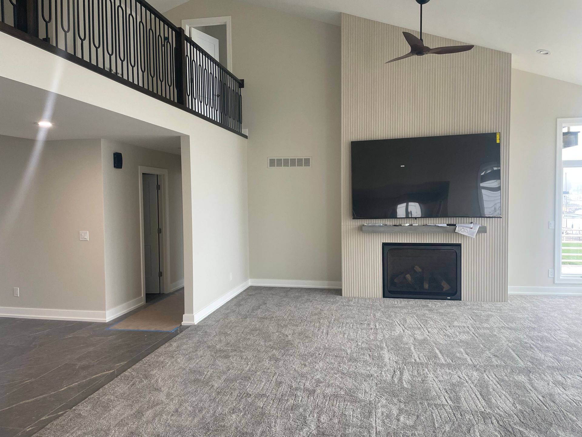 Empty living room with gray carpet, fireplace, TV, and upstairs balcony railing