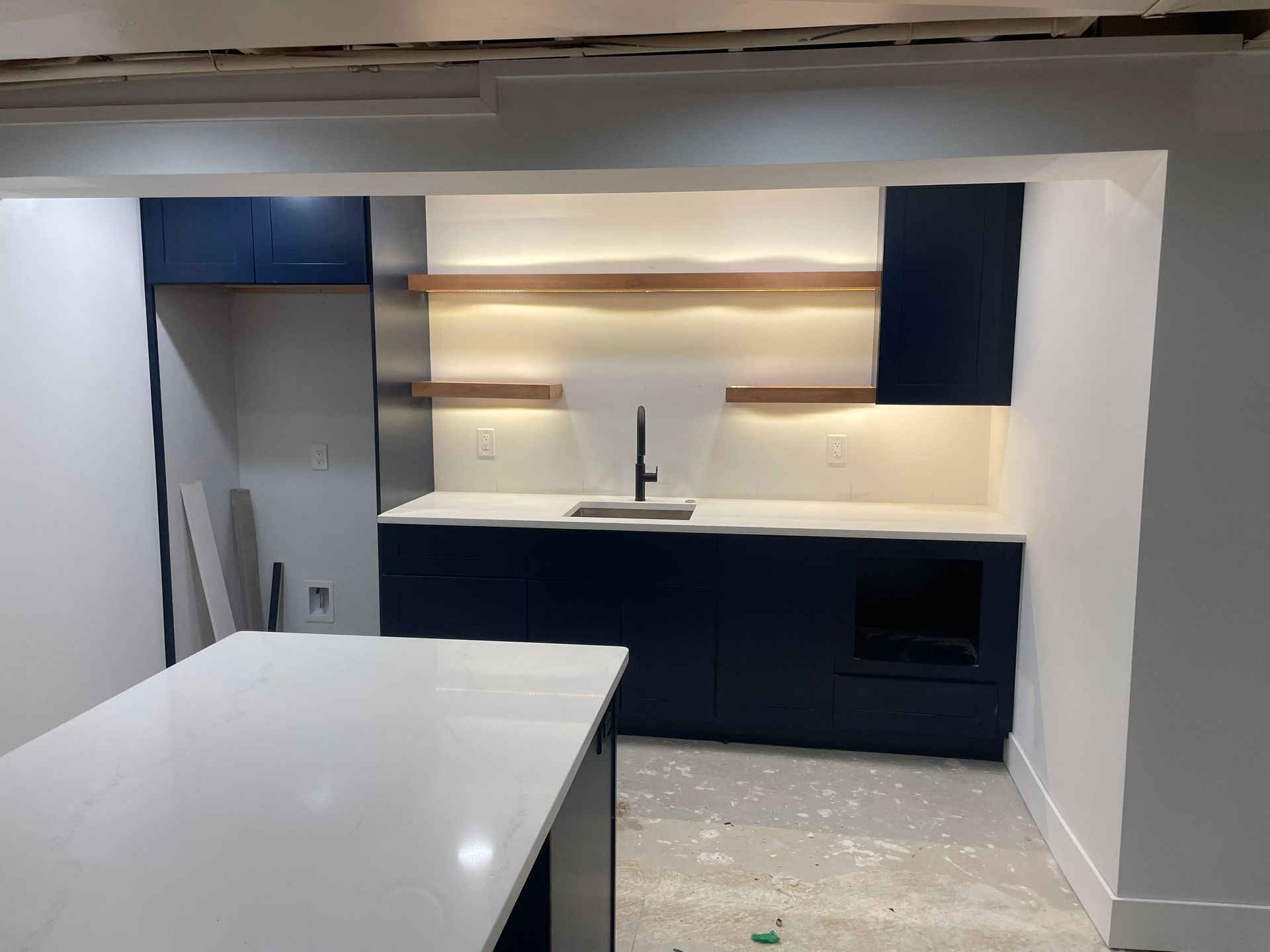 Modern kitchen with dark cabinets, white countertops, and open shelving under warm lights