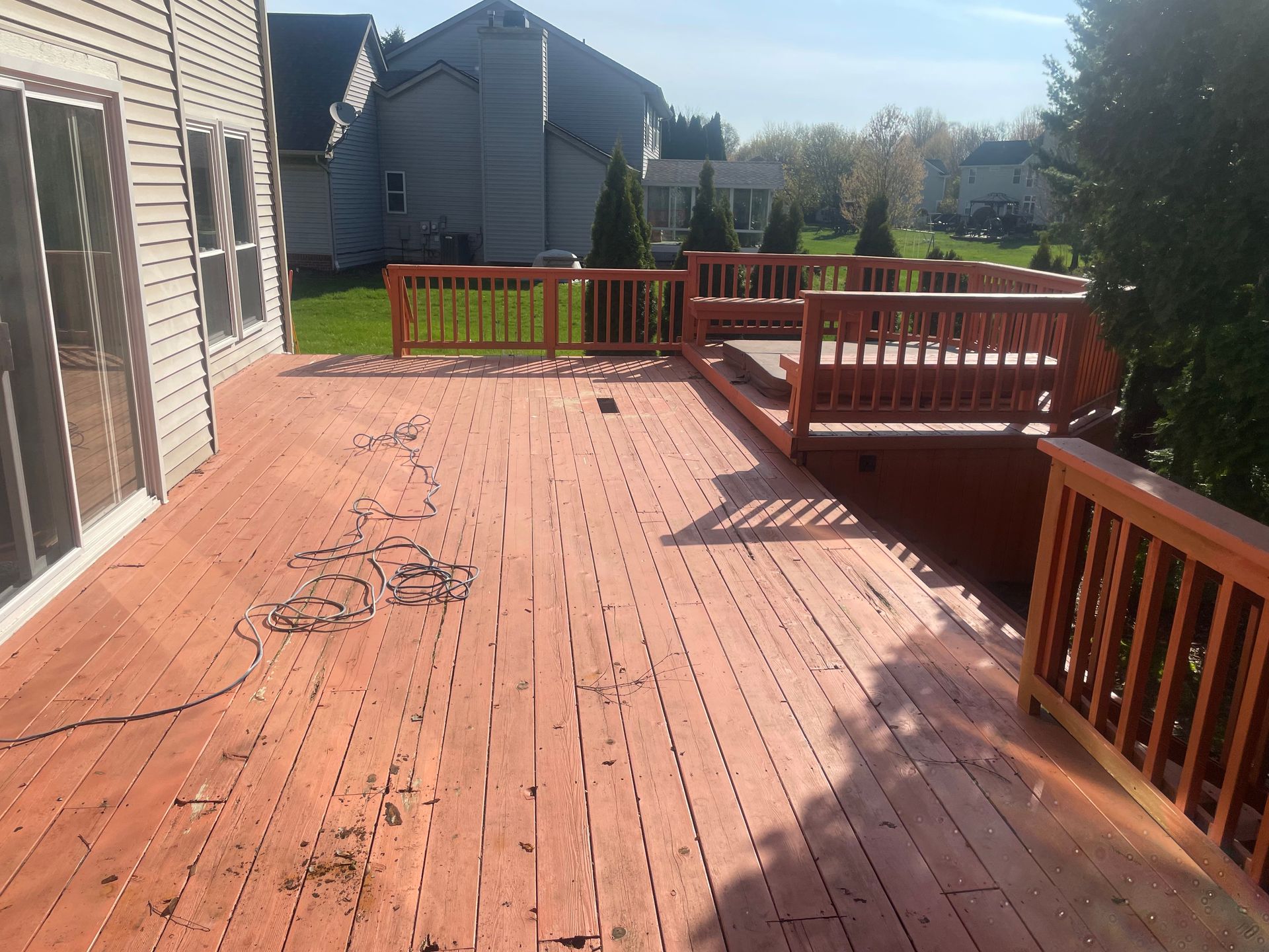 Wooden deck with red railings beside a house, overlooking a yard on a sunny day