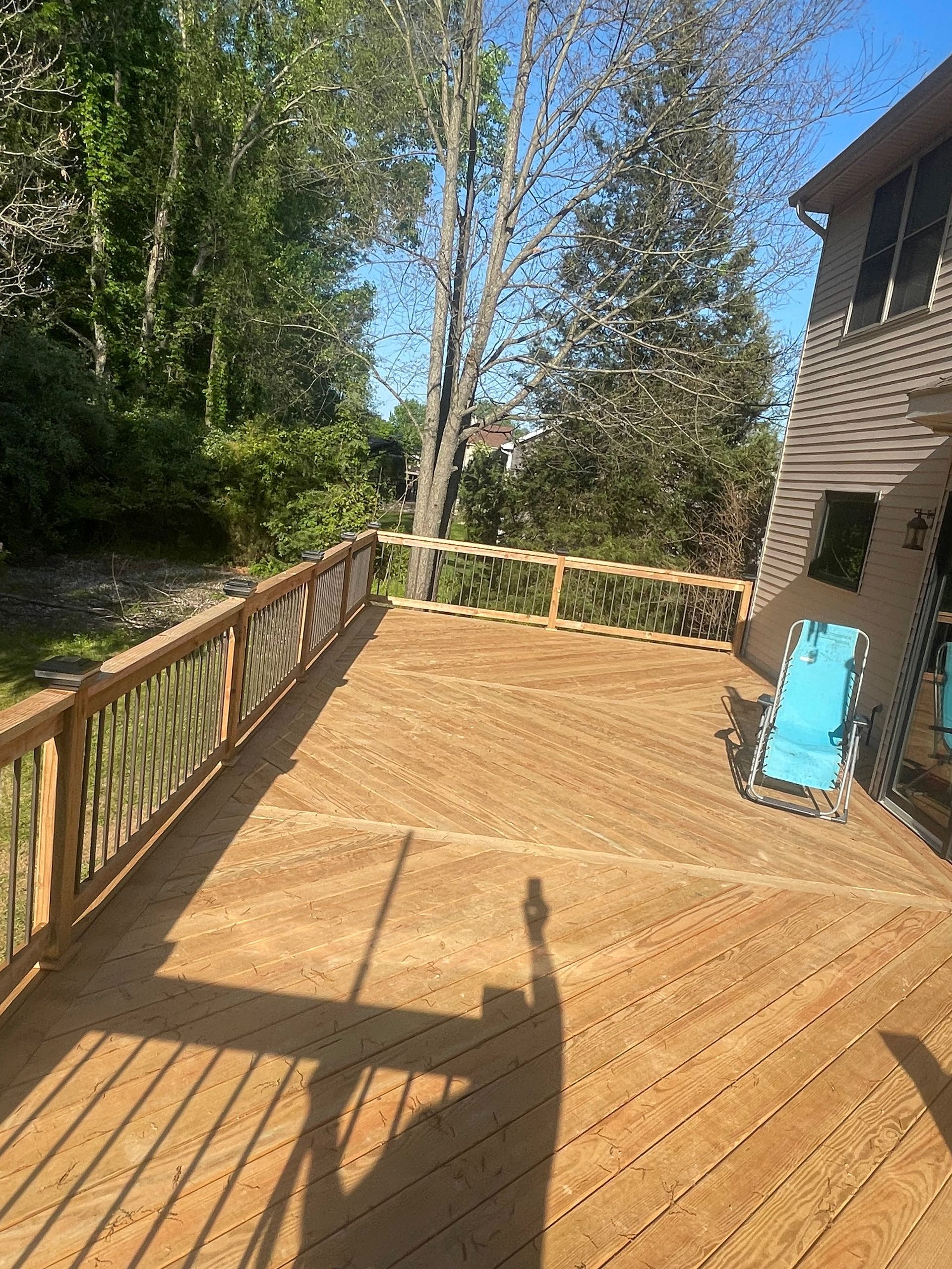 Wooden deck beside a house, with railing, trees, and a blue board leaning against the wall.