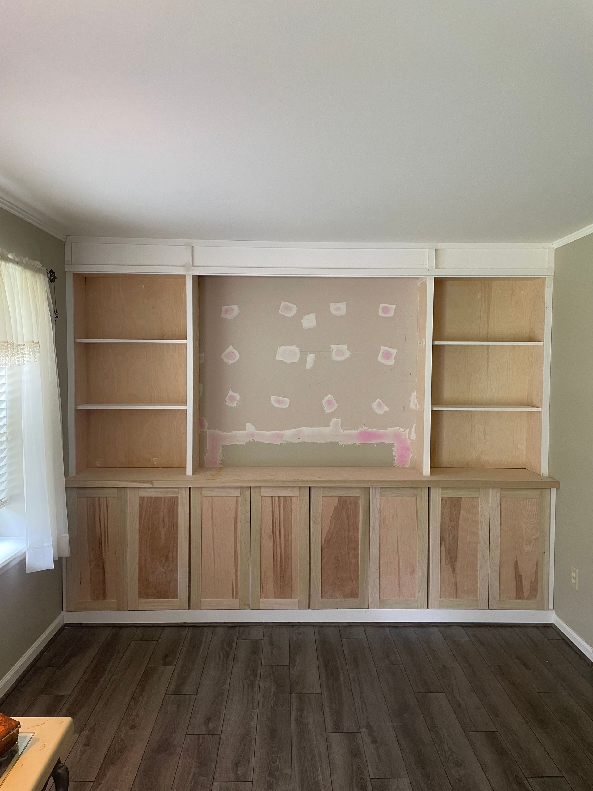 Built-in wooden cabinets and shelves around a pink wallpapered wall in a living room.