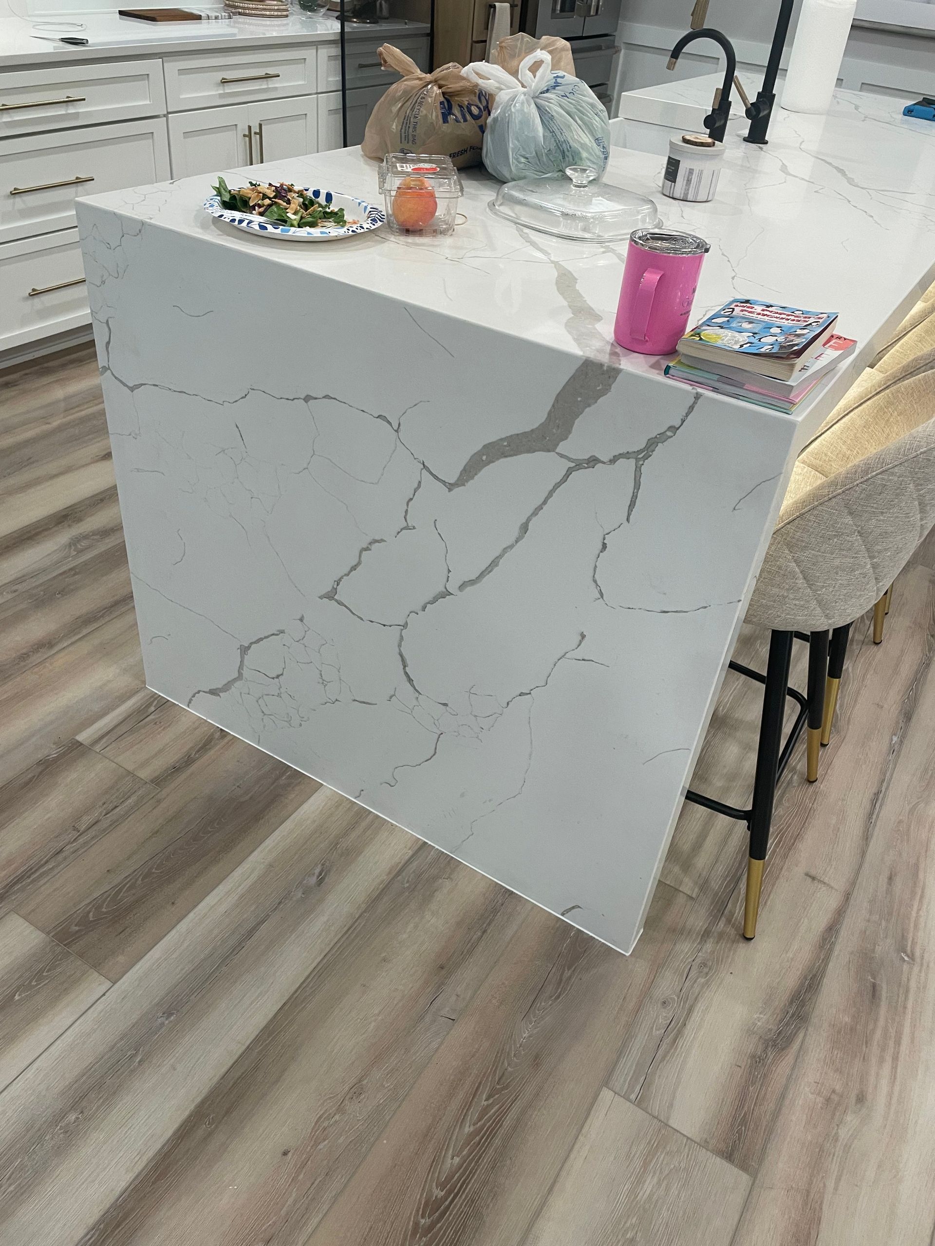 White marble kitchen island with items on top, in a modern room with wood flooring.