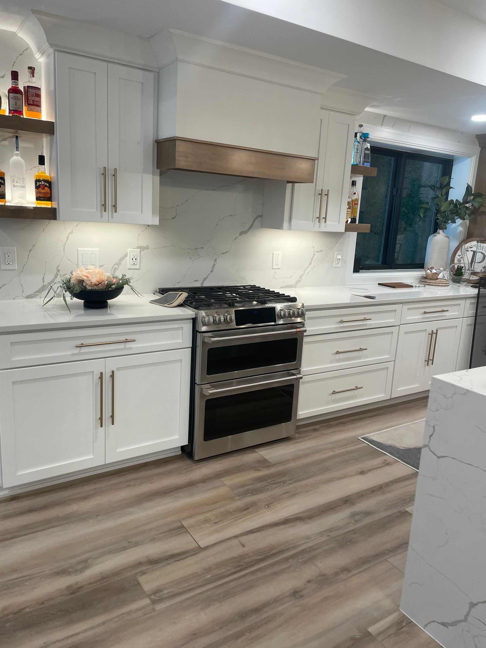 Modern white kitchen with black stove, wood floor, and window above the sink.