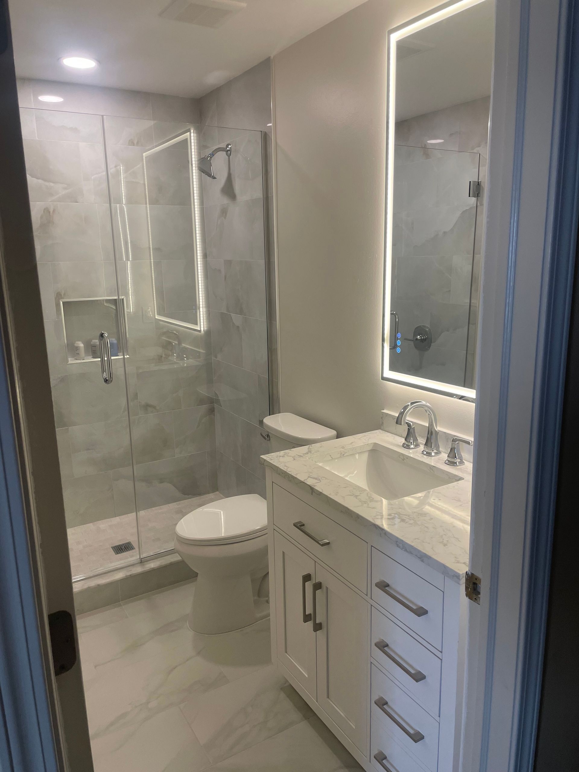 Small modern bathroom with glass shower, toilet, vanity sink, and white tile walls.