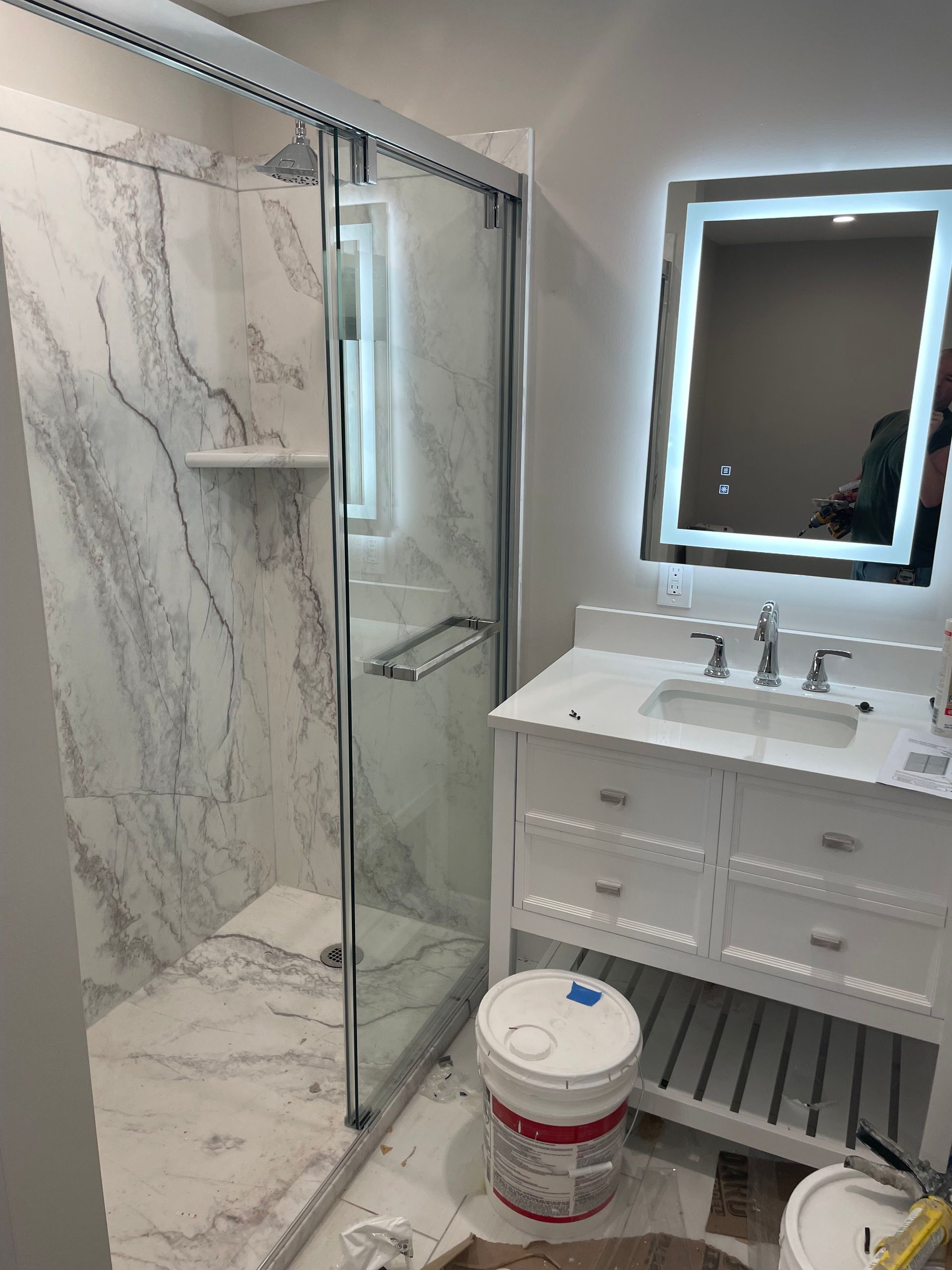 Modern bathroom with marble shower, glass door, white vanity, and mirror lit by LED lighting