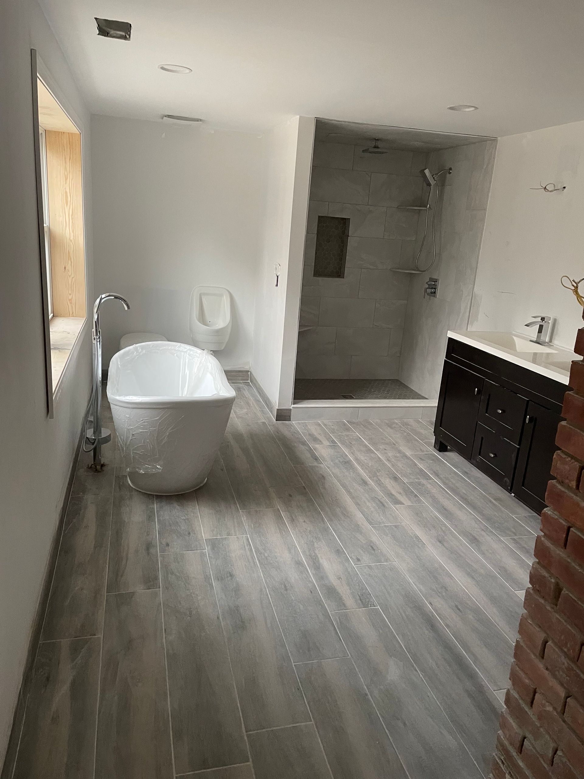 Modern bathroom with freestanding tub, walk-in shower, and dark vanity on gray wood-look flooring