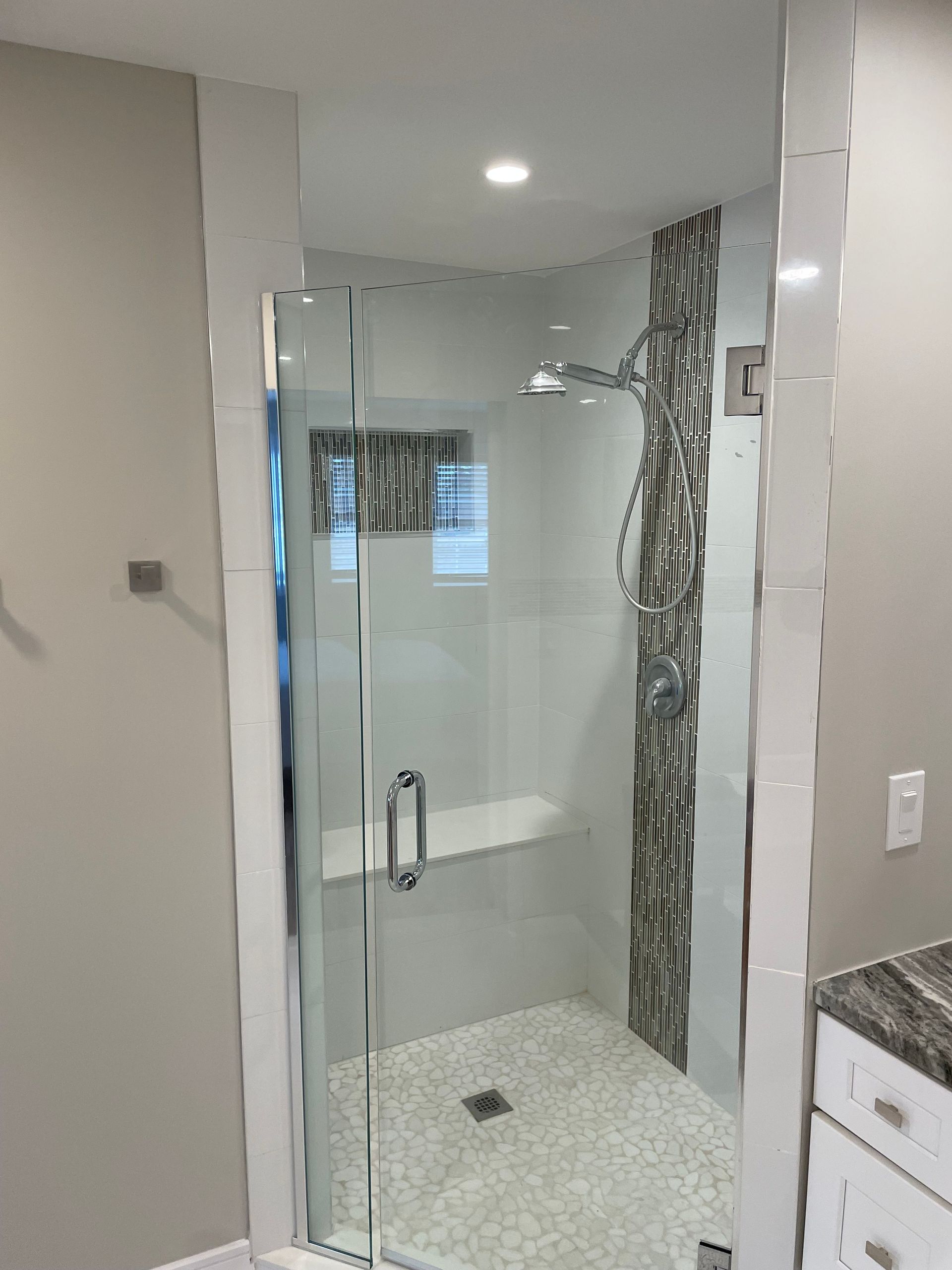 Glass walk-in shower with white tile floor and patterned accent wall in a bathroom