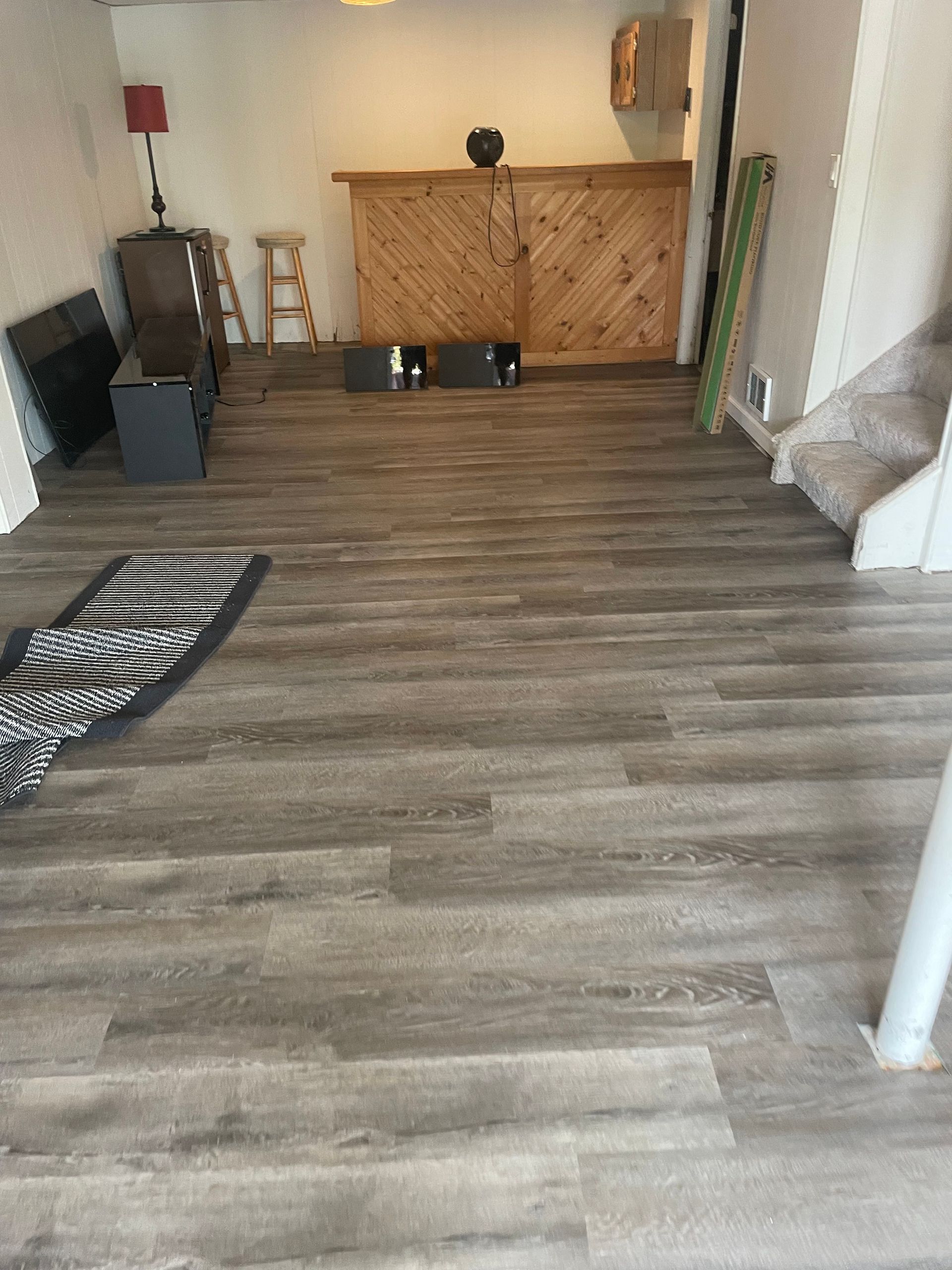 Empty living room with gray wood flooring, a small bar counter, and a black-and-white rug.