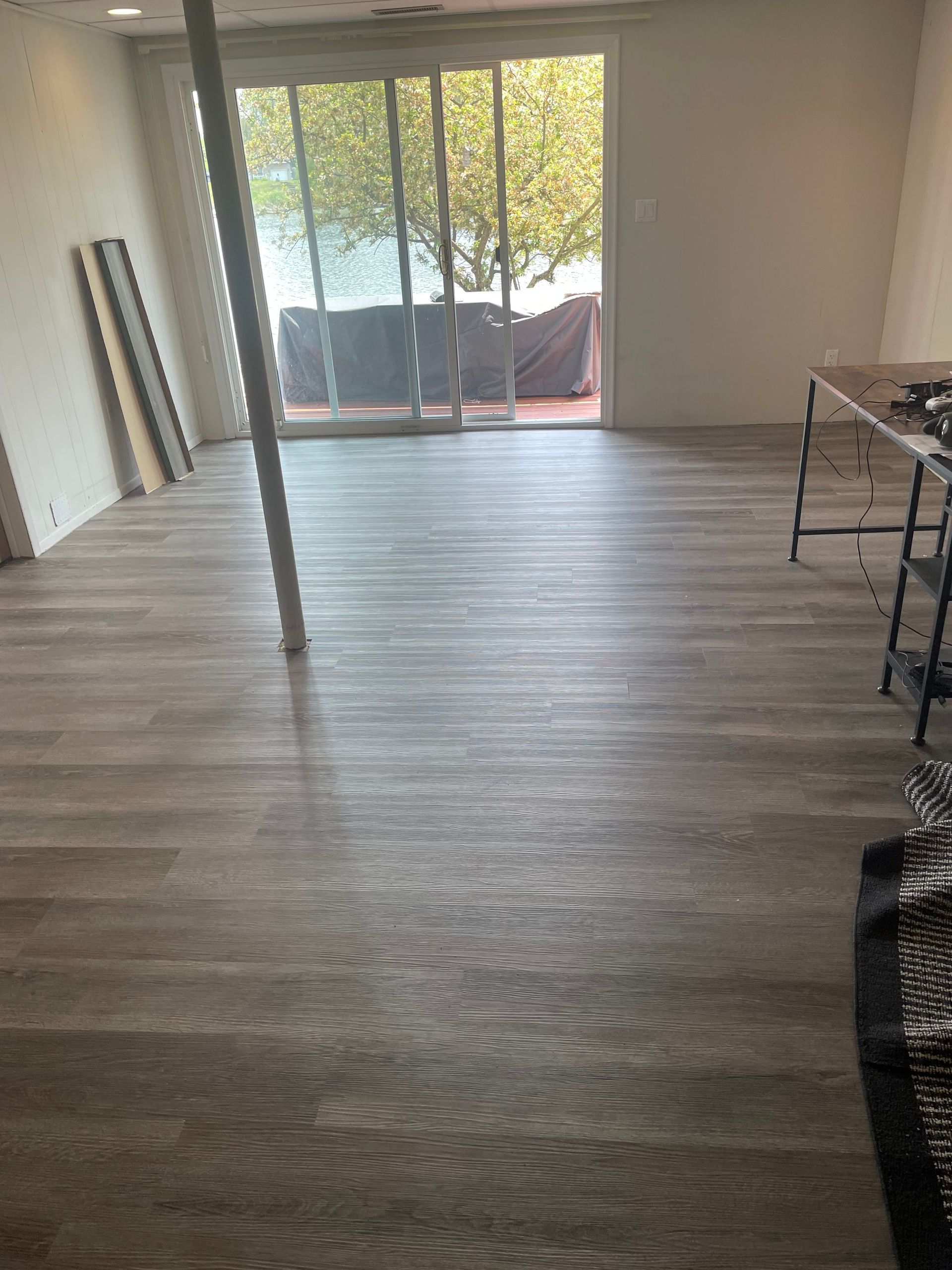 Empty room with gray wood-look flooring, sliding glass doors, and rolled materials leaning against the wall.