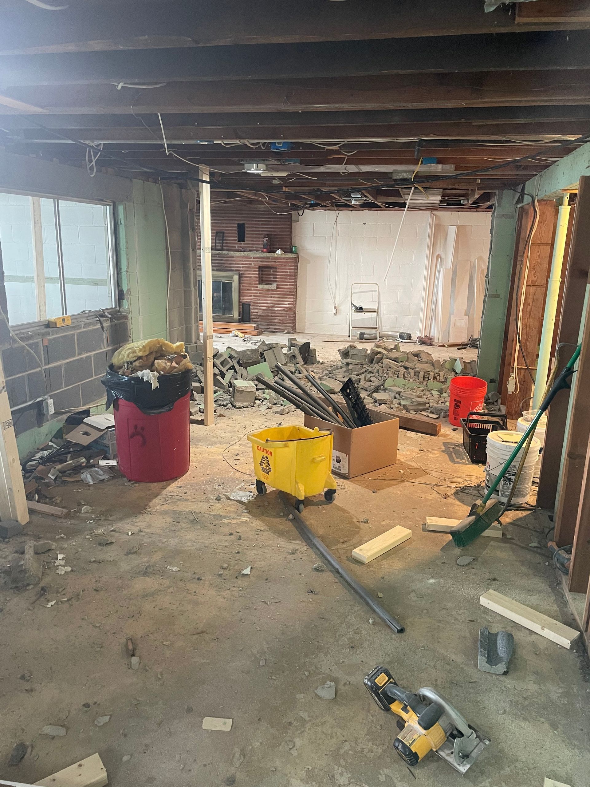 Basement under renovation with exposed beams, debris, tools, and construction materials scattered around.
