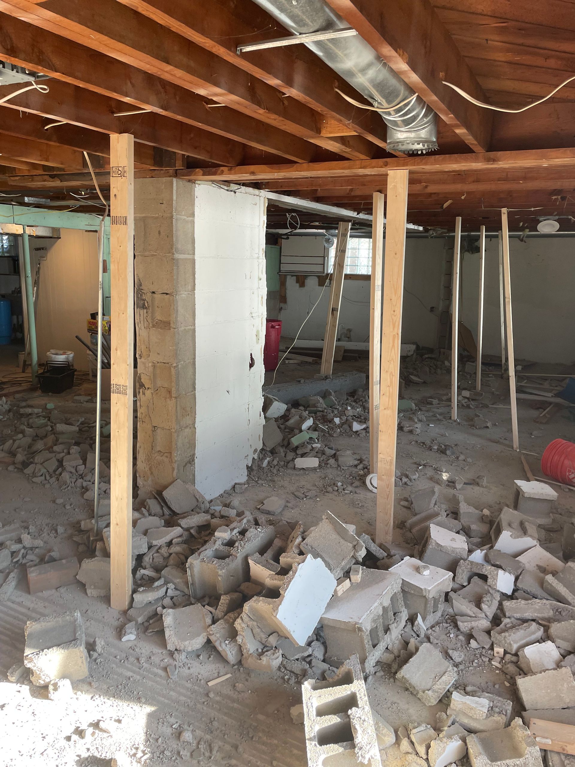 Basement under demolition with exposed wooden beams, support posts, and piles of broken concrete and debris
