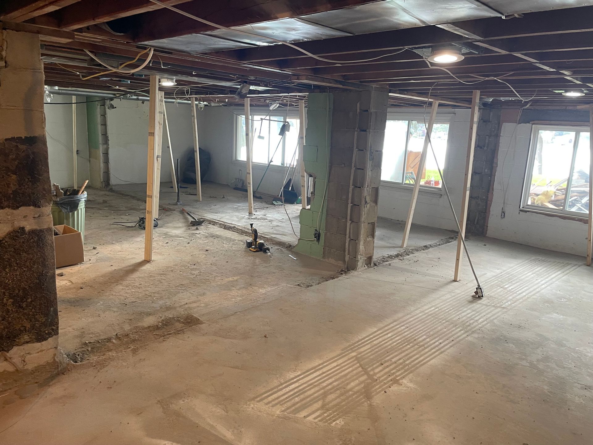 Empty unfinished room with exposed ceiling beams, support posts, and sunlight through windows.