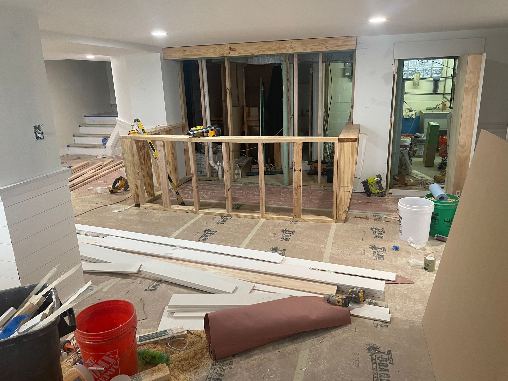 Partially renovated room with exposed wall studs, scattered boards, and construction tools on the floor
