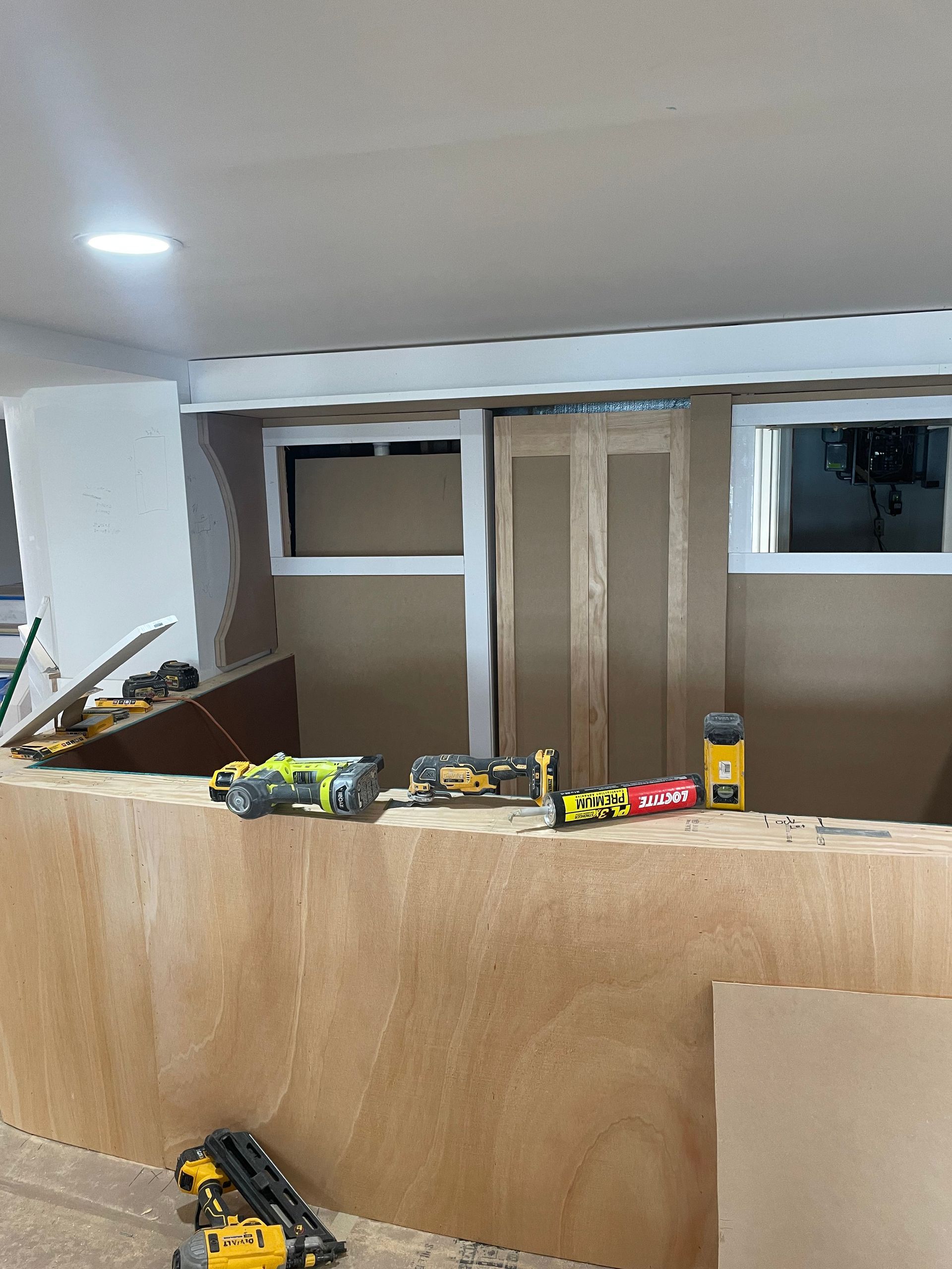 Toys and construction pieces scattered on a wooden barrier in a room under renovation, with windows and bare walls.
