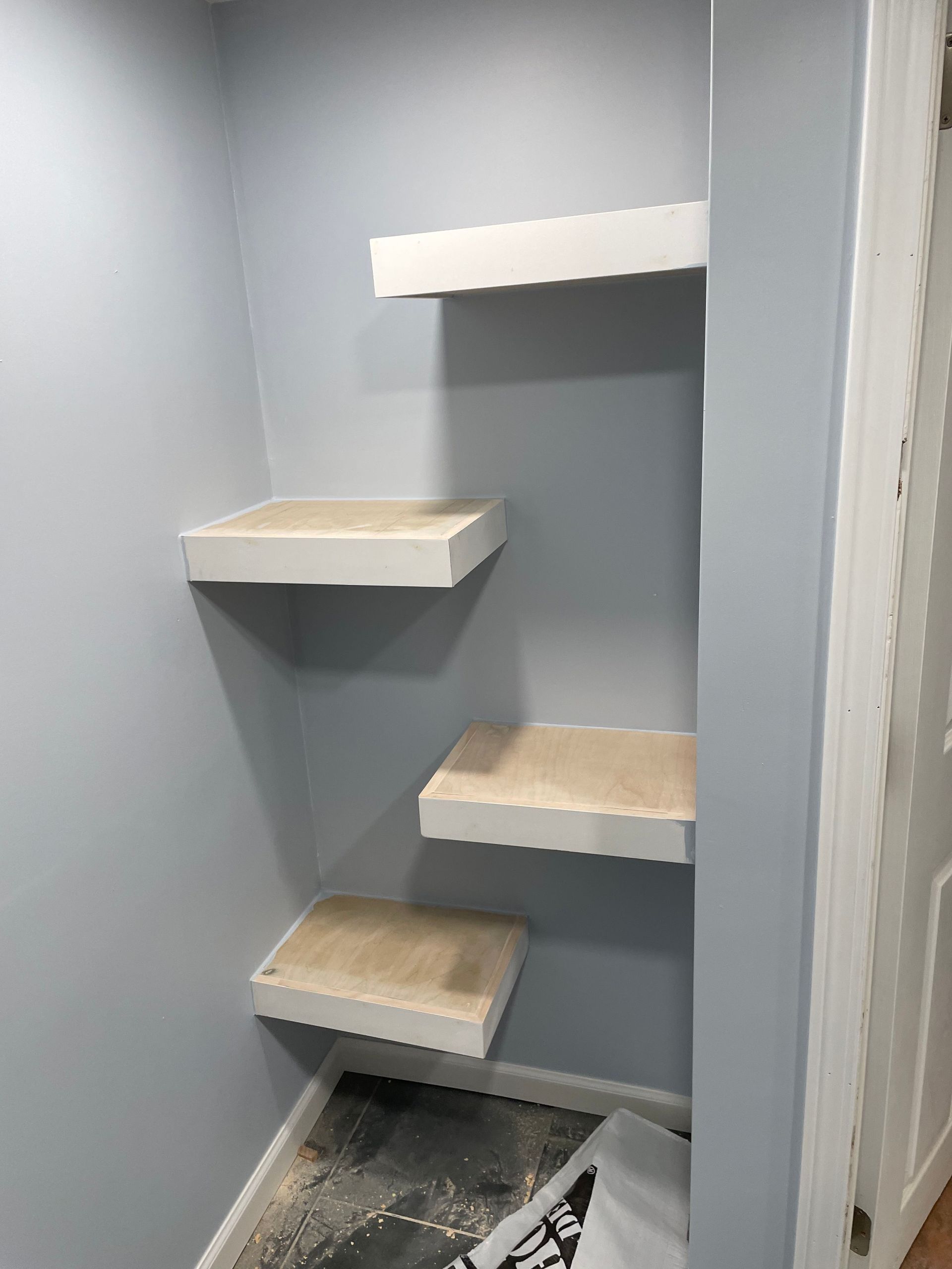 Small gray closet with four wall shelves and a floor opening below.