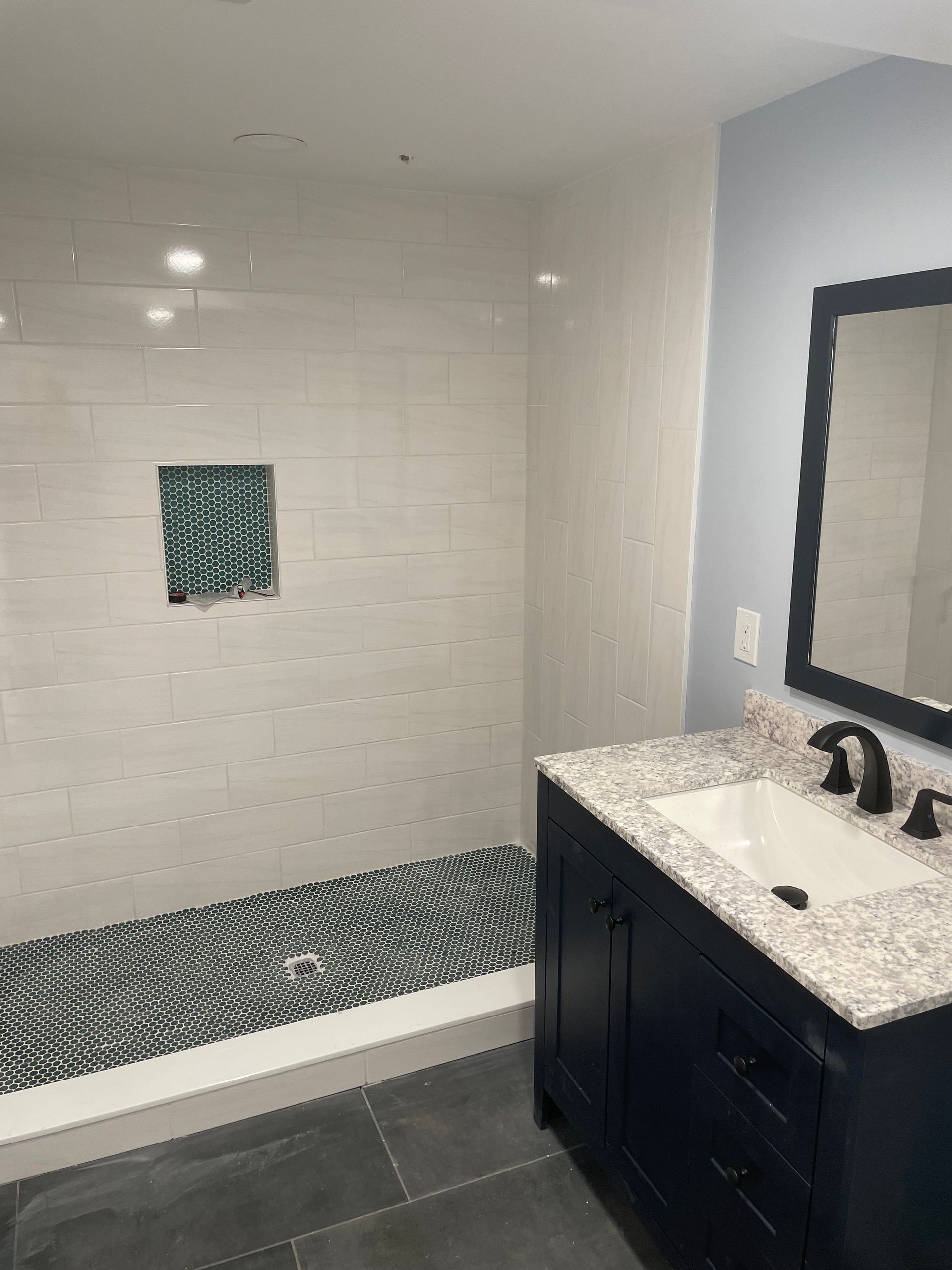 Bathroom with white tiled tub and shower, dark vanity, and large mirror.