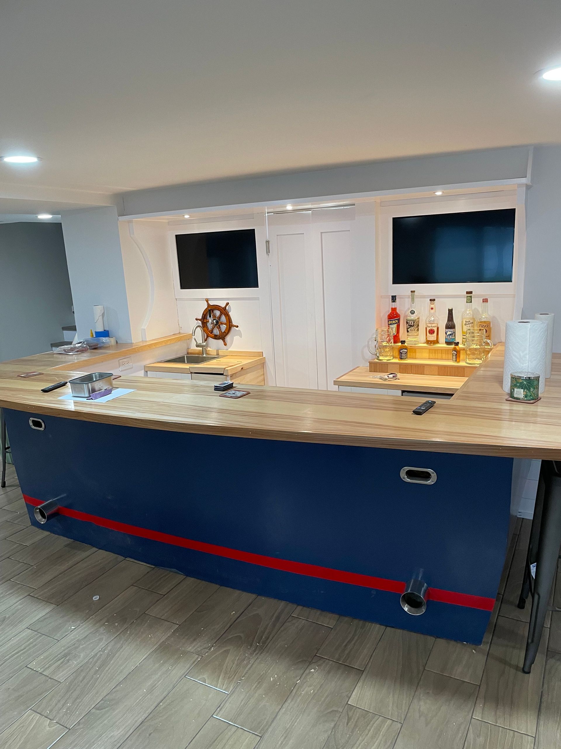 Home bar with blue front panel, wooden countertop, and bottles on a lit serving area