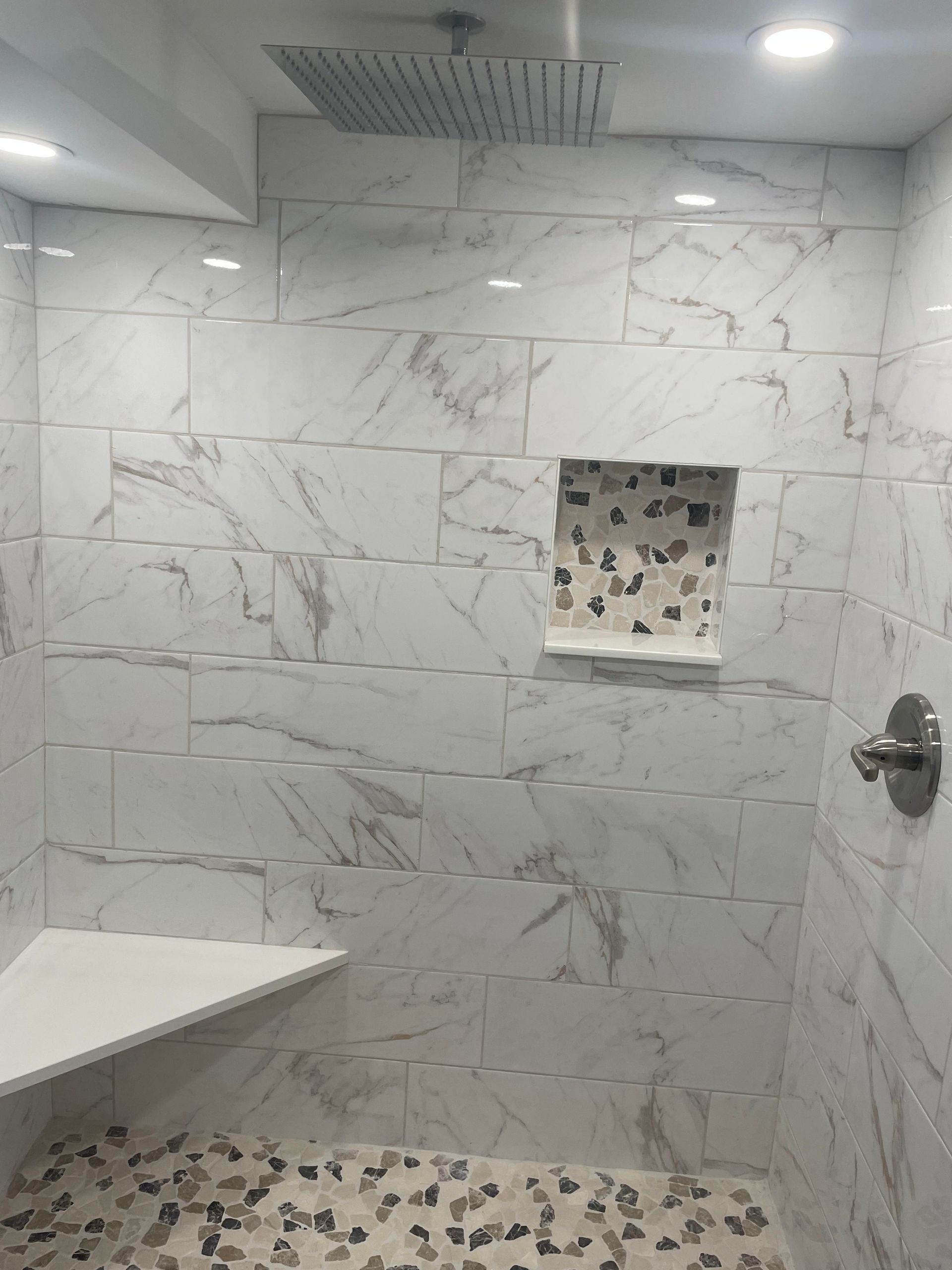 Modern bathroom with white marble-pattern tile, tiled shower wall niche, and patterned floor.