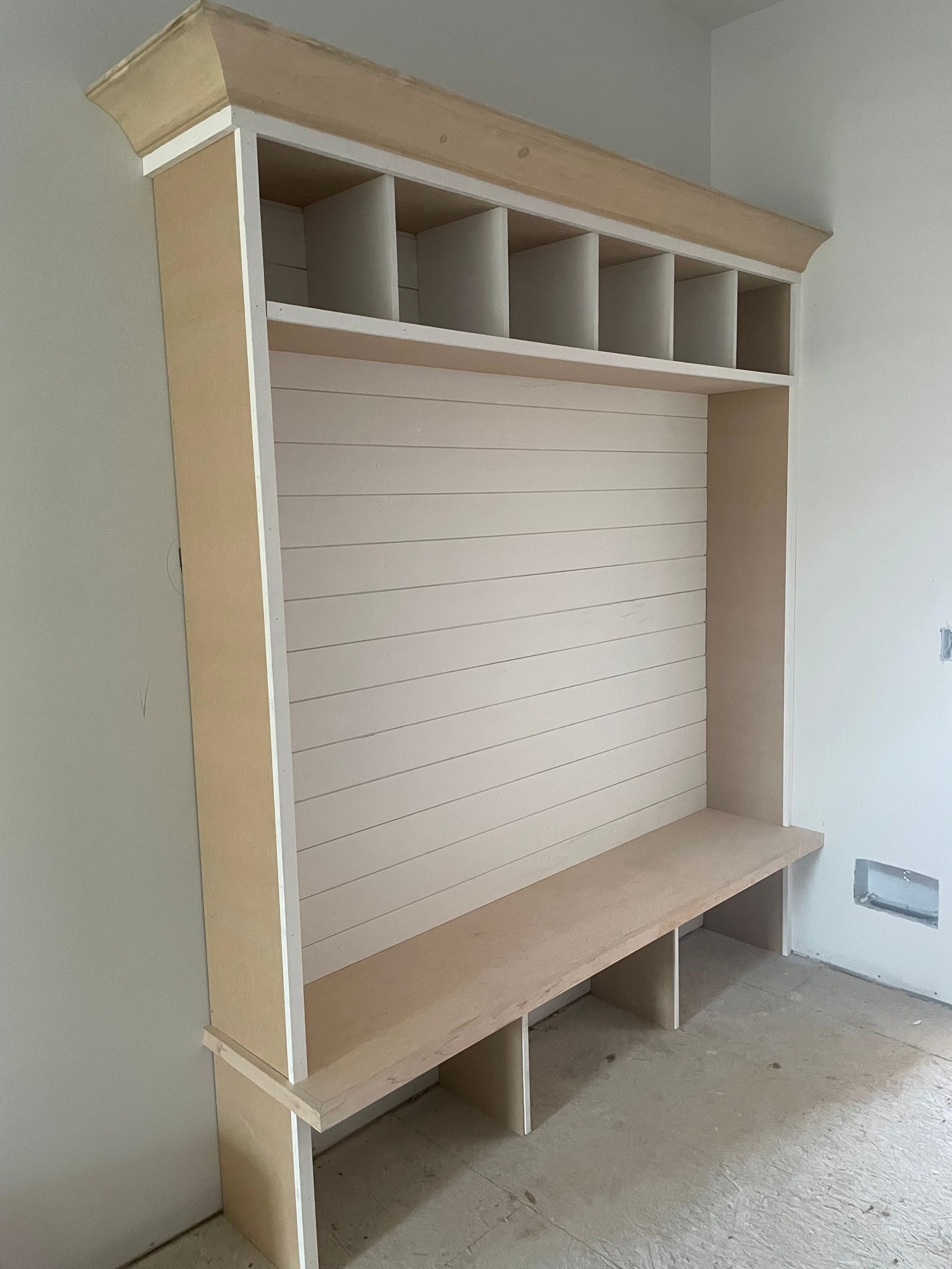 Wooden mudroom bench with cubbies and wall-mounted pegboard in a blank room