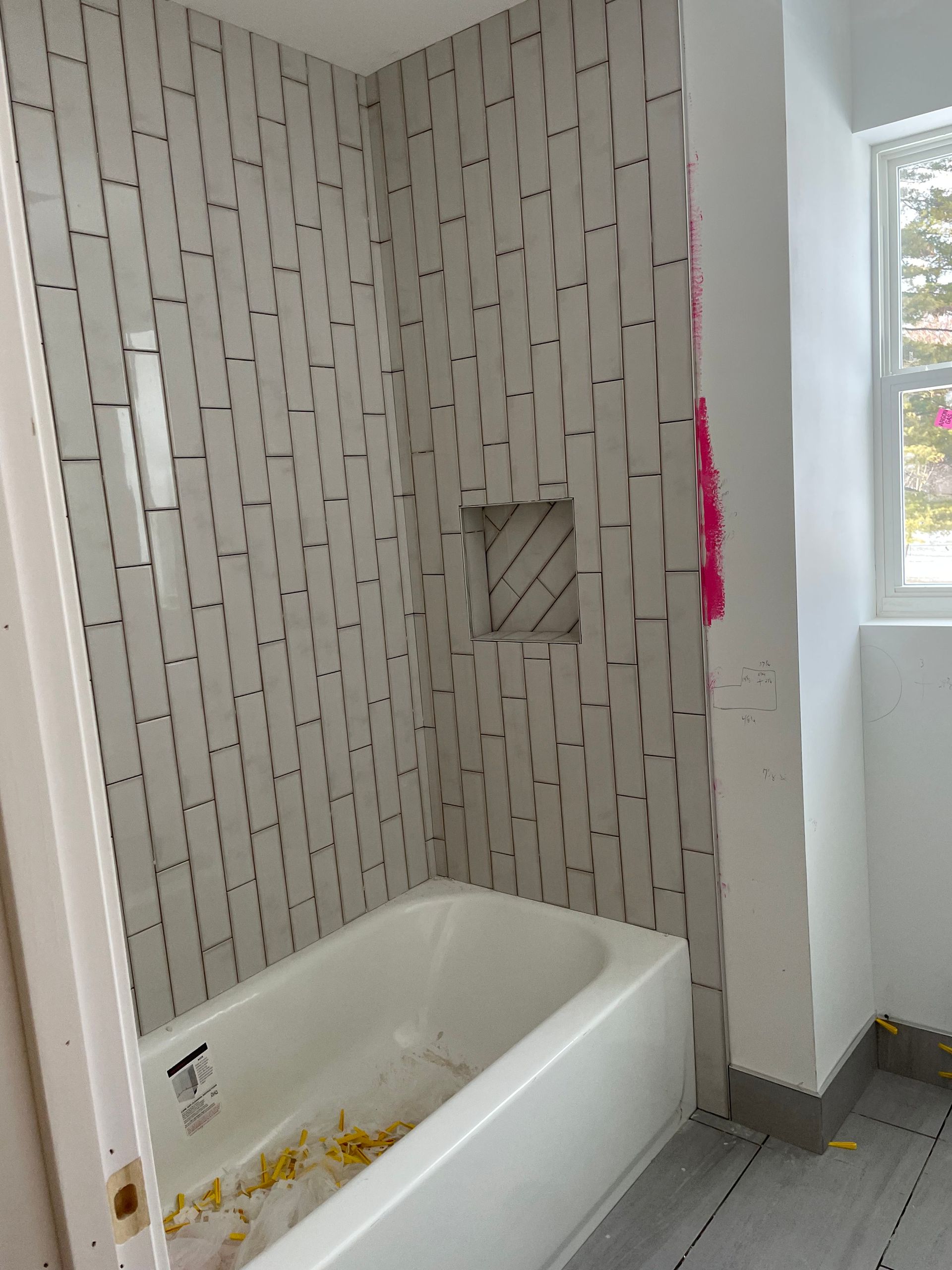 Bathroom with a white tub, tiled shower walls, and a window letting in daylight.