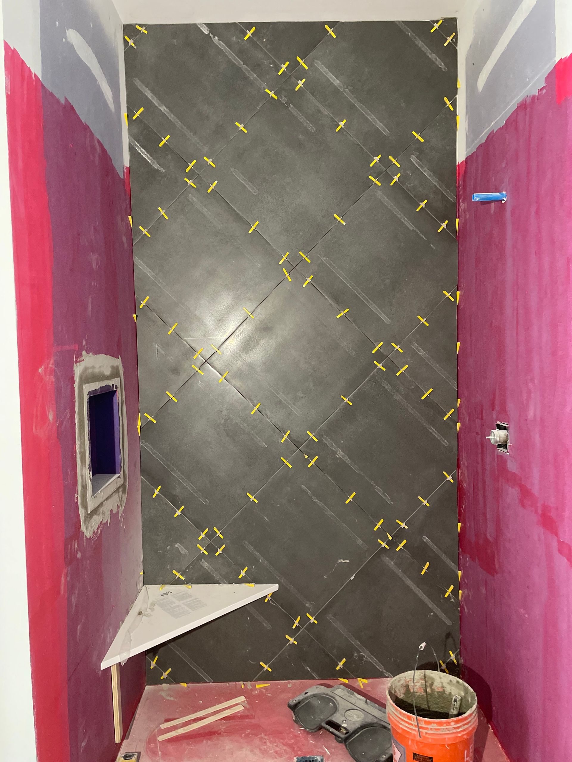 Narrow hallway under renovation with pink walls, gray tiled floor, a bucket, and construction debris.